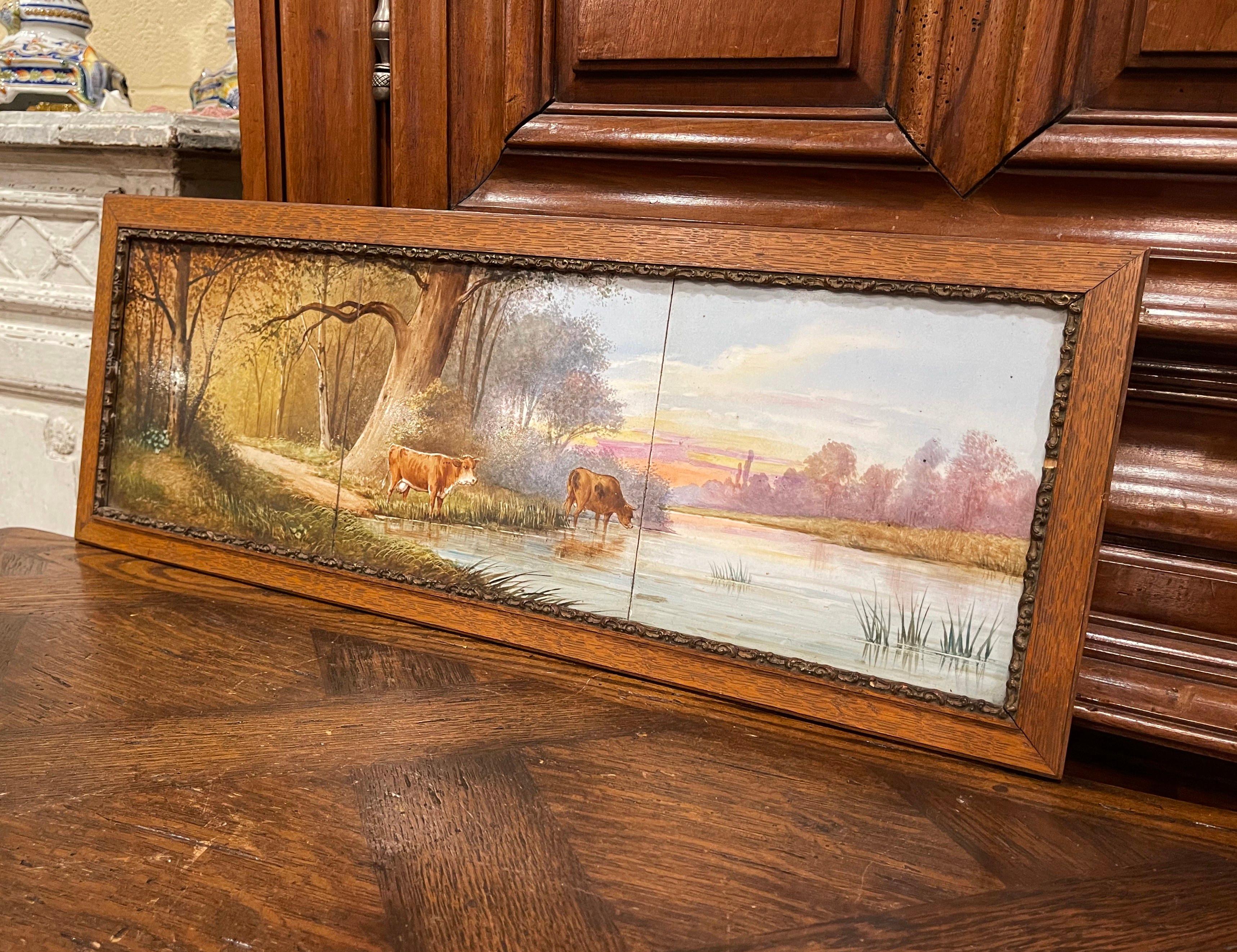Decorate a kitchen wall with this elegant framed tile painting. Crafted in France circa 1860 and rectangular in shape, the subject matter depicts a bucolic pastoral scene at dawn with cows drinking in a river with pasture around. The three antique