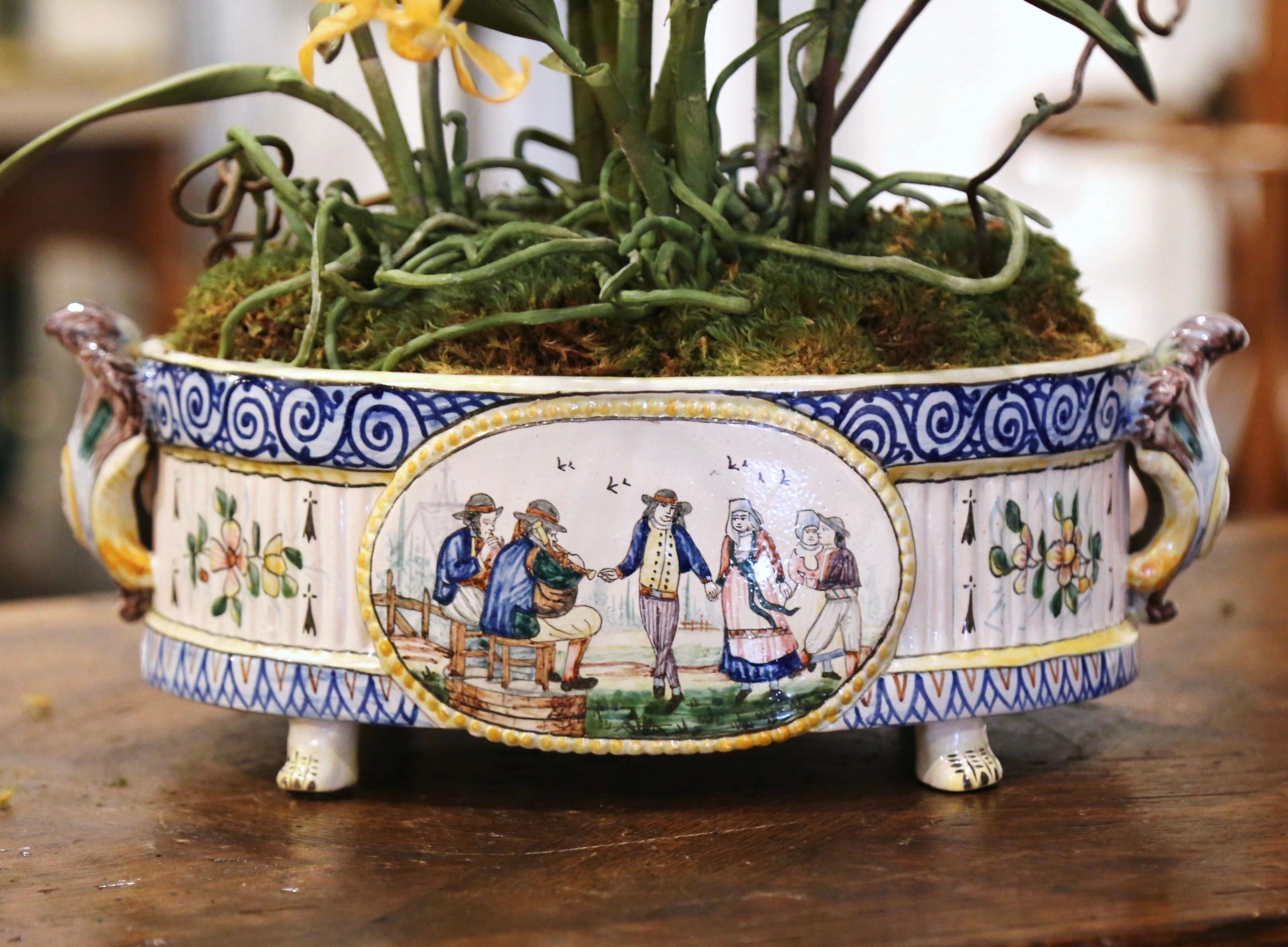 Complete your faience collection with this colorful antique cachepot from Brittany. Crafted in Quimper, France, circa 1880 and oval in shape, the jardinière with acanthus leaf handles stands on four paw feet; on each side, the ceramic planter