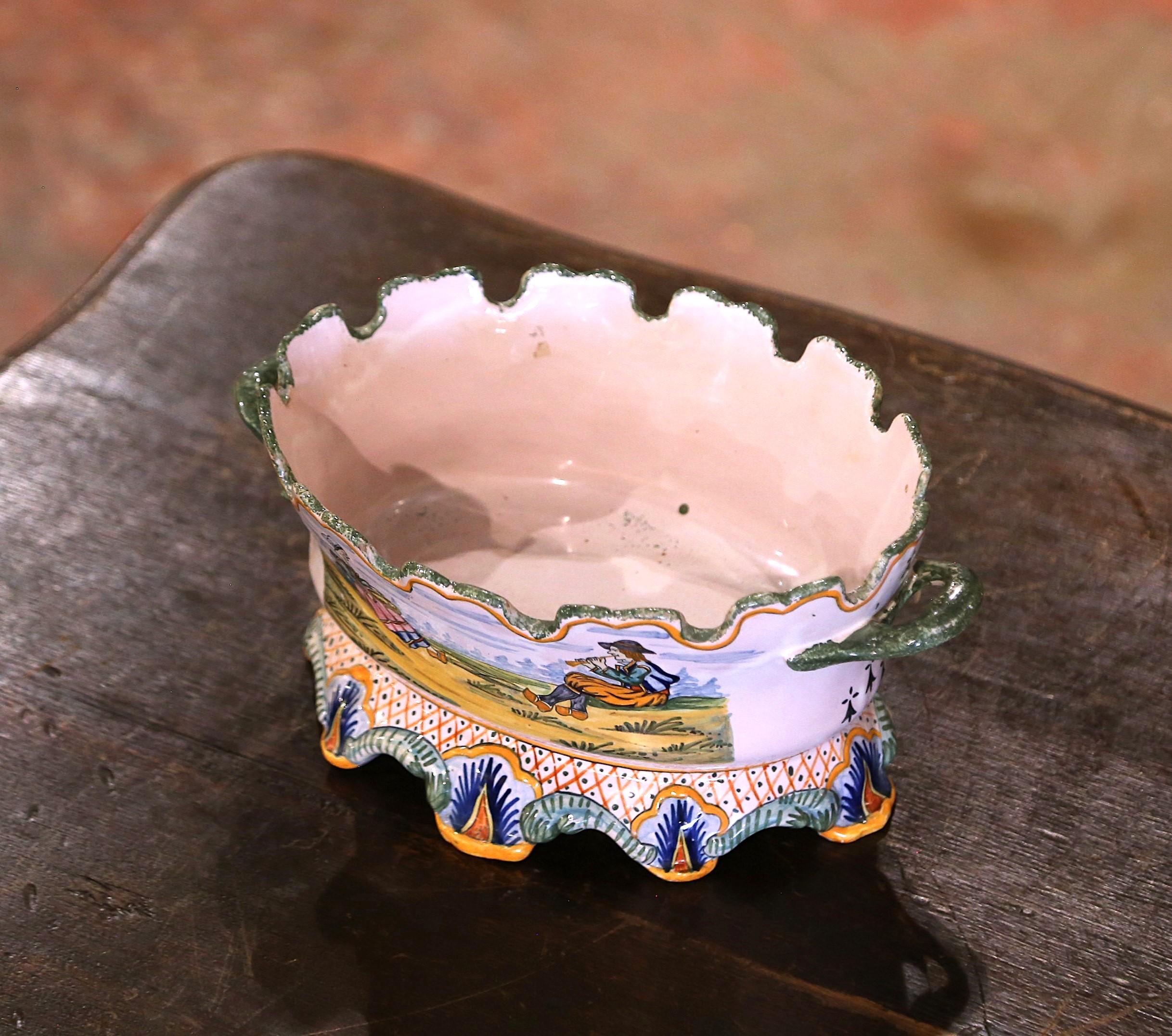Decora un bufé o una mesa con esta colorida jardinera de loza antigua. Fabricada en Bretaña, Francia, hacia 1880, la jardinera ovalada presenta bordes festoneados en forma de corona y está adornada con asas laterales. La decoración representa dos