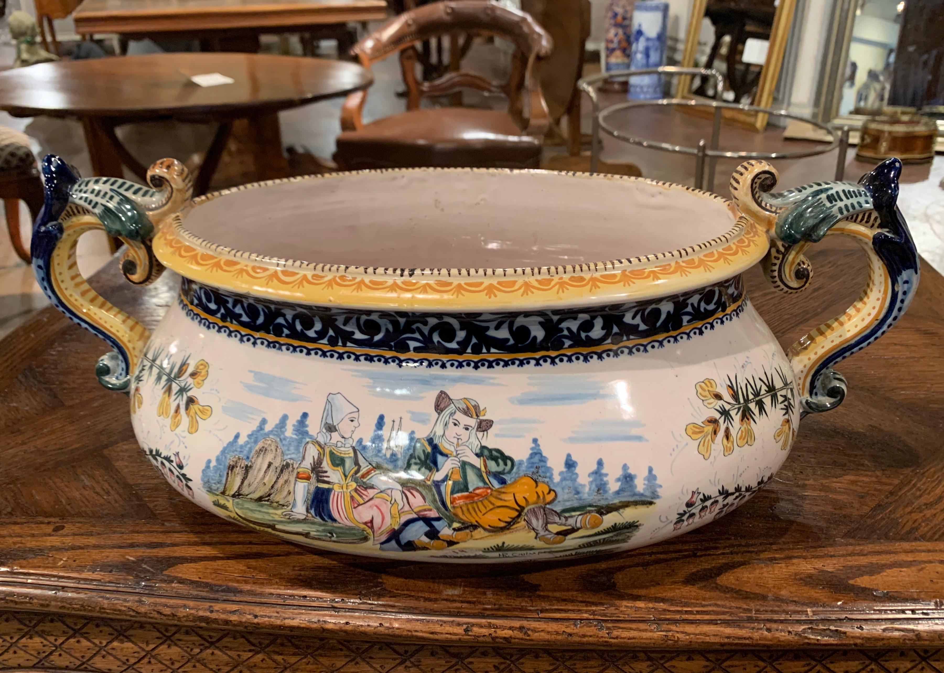 This large and colorful oval cachepot was sculpted in Brittany, France, circa 1890. The uniquely shaped pot has a large mouth, two side handles, and is relatively shallow in depth. The hand painted jardinière features a Classic Briton couple dressed