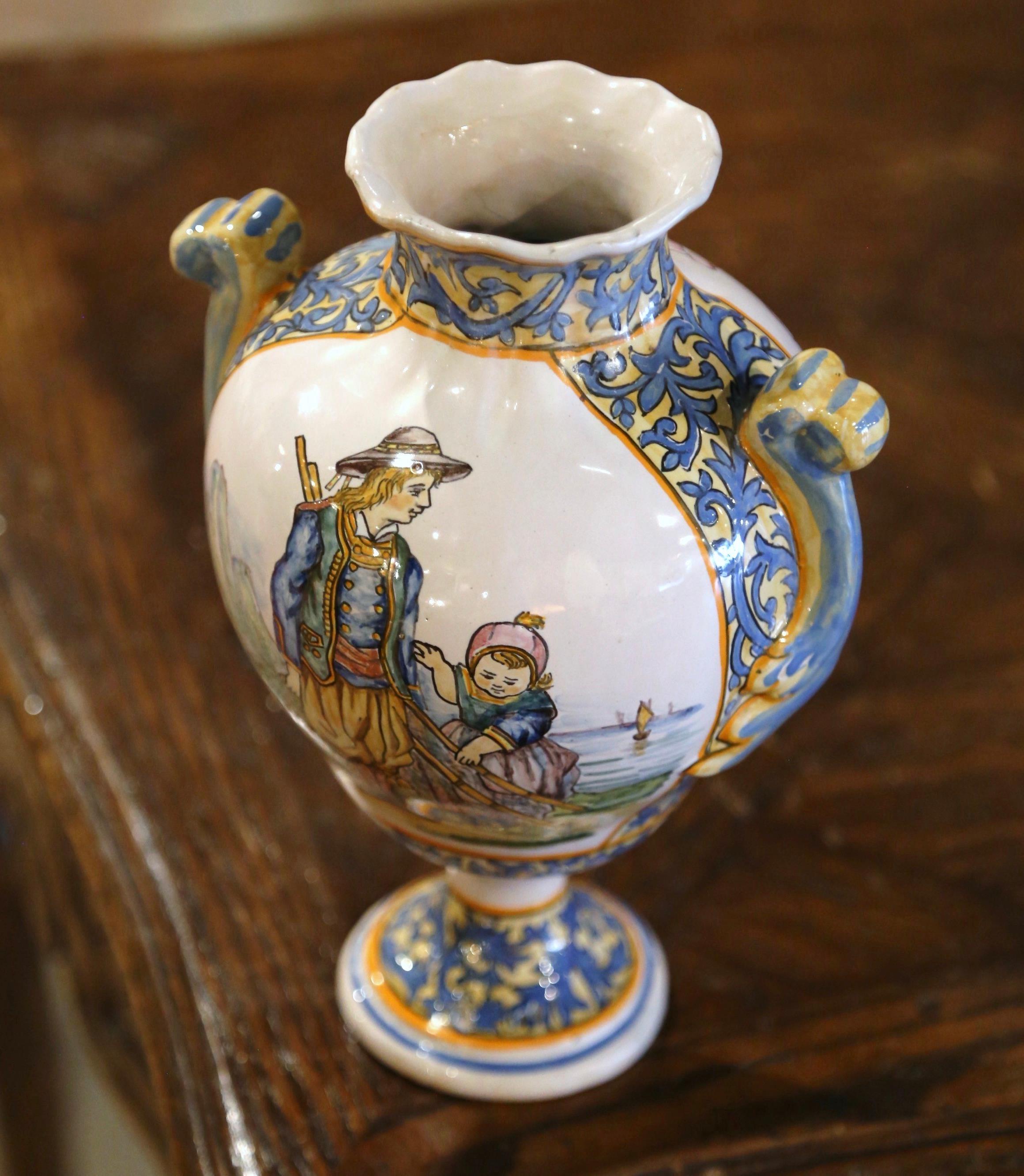 Created in Brittany, France circa 1895, the hand painted faience vase is round in shape with scalloped edges at the rim. The vessel with side handles is decorated at the center with a Breton and his kid going fishing, and dressed in traditional