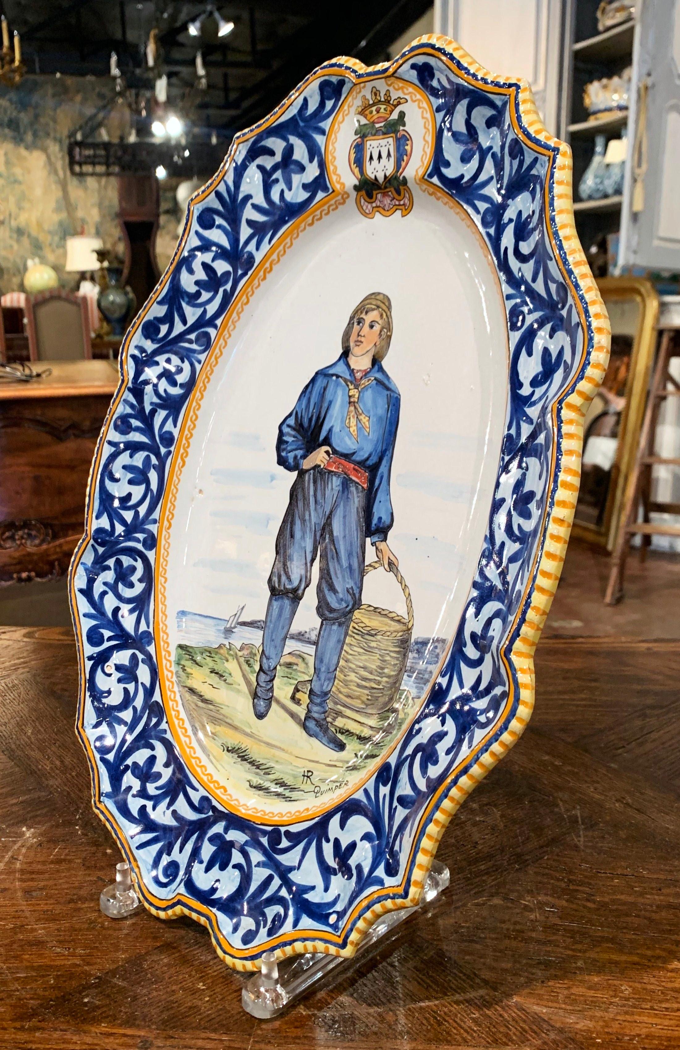 Décorez un mur ou une étagère avec ce grand plat ancien. Créée en Bretagne (France) vers 1895, cette assiette en céramique peinte à la main représente un Breton en costume traditionnel partant à la pêche aux moules. Le plat ovale en porcelaine est