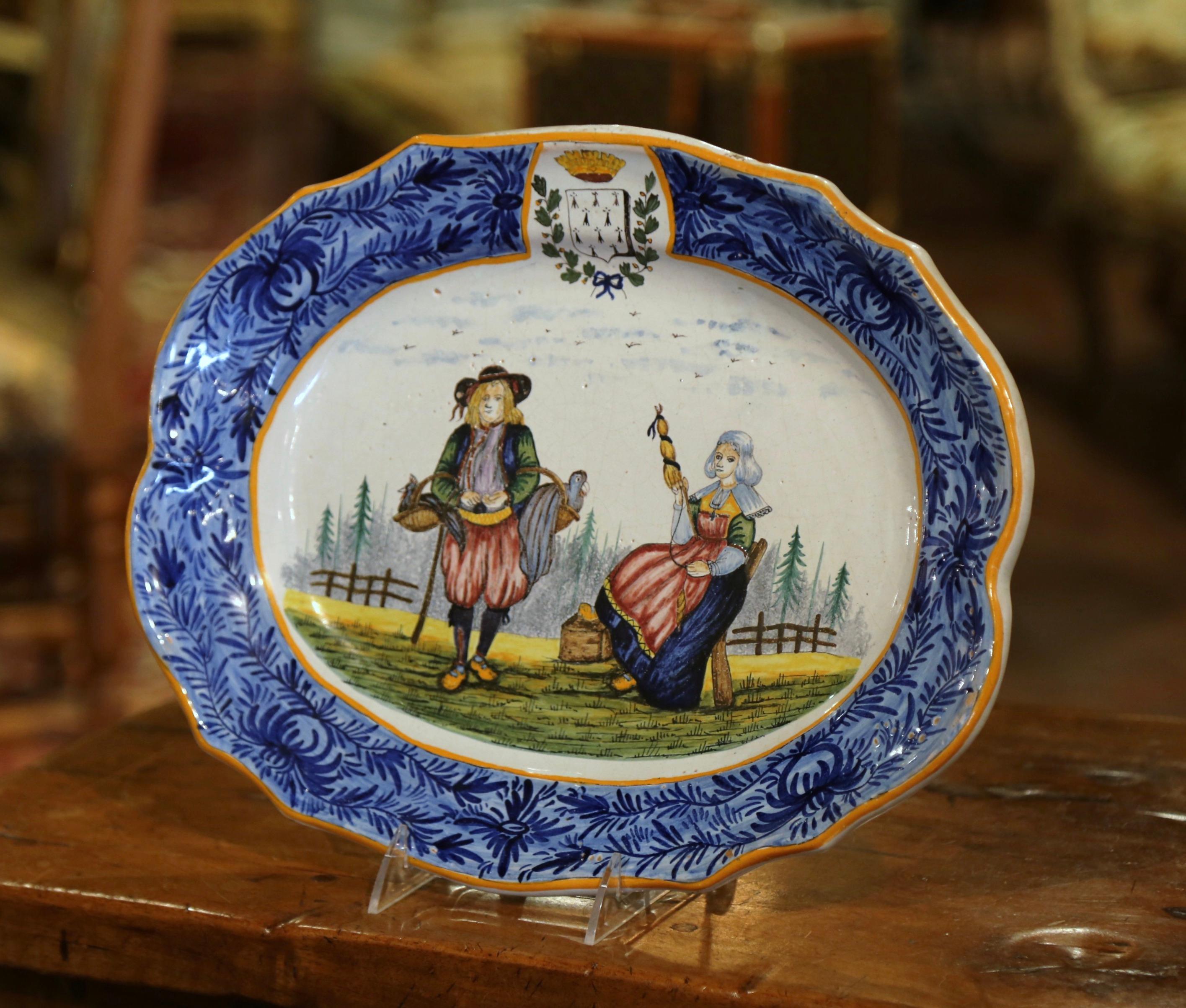 Dekorieren Sie eine Wand oder ein Regal mit dieser farbenfrohen antiken Platte. Der große handbemalte Keramikteller wurde um 1895 in der Bretagne, Frankreich, hergestellt und zeigt ein bretonisches Paar in traditioneller Tracht. Der ovale
