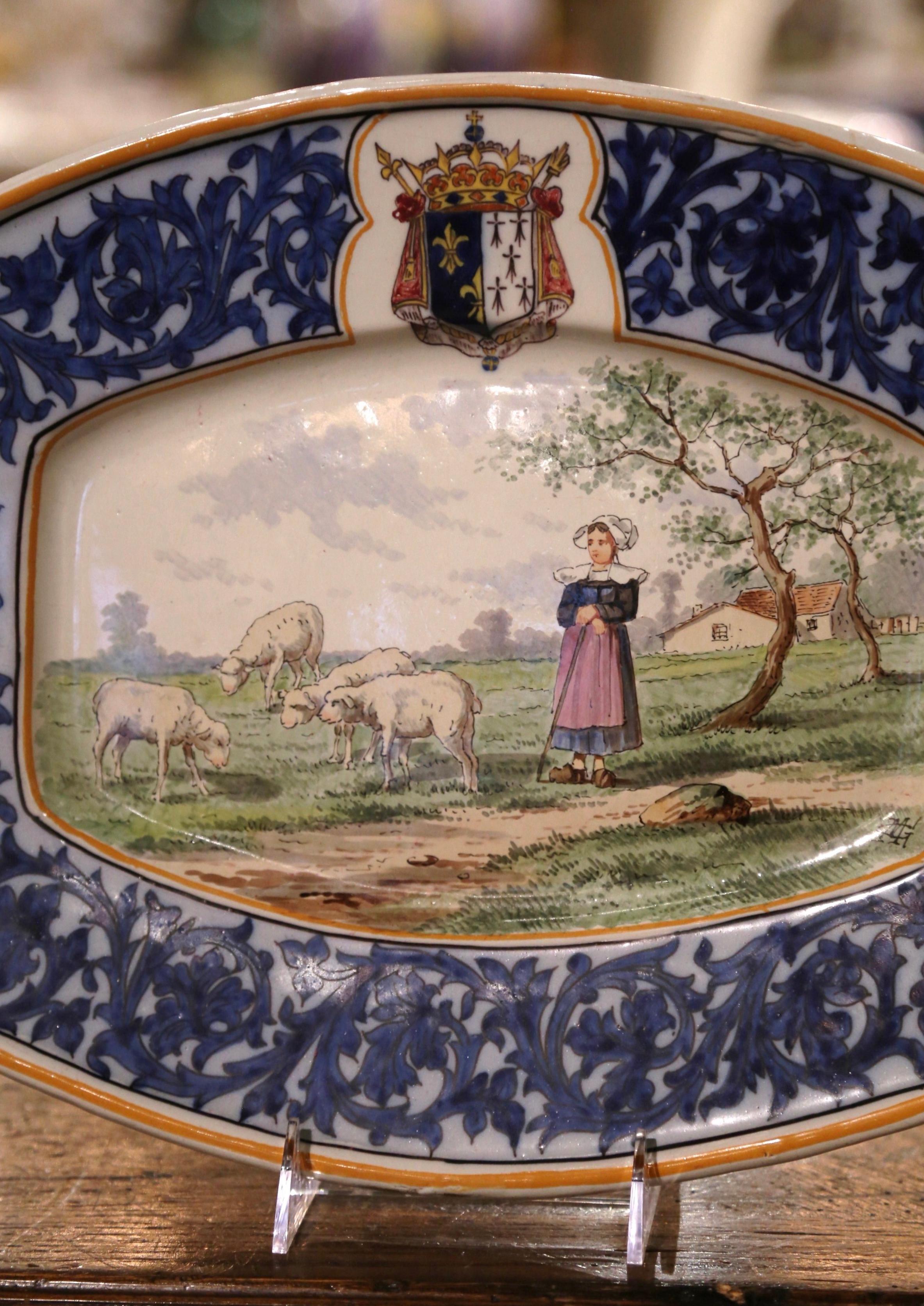 Decorate a wall or a shelf with this colorful antique platter. Created in Brittany, France circa 1895, the large hand painted ceramic plate depicts a pastoral scene with a Breton peasant in traditional costumes attending her sheep. The oval,