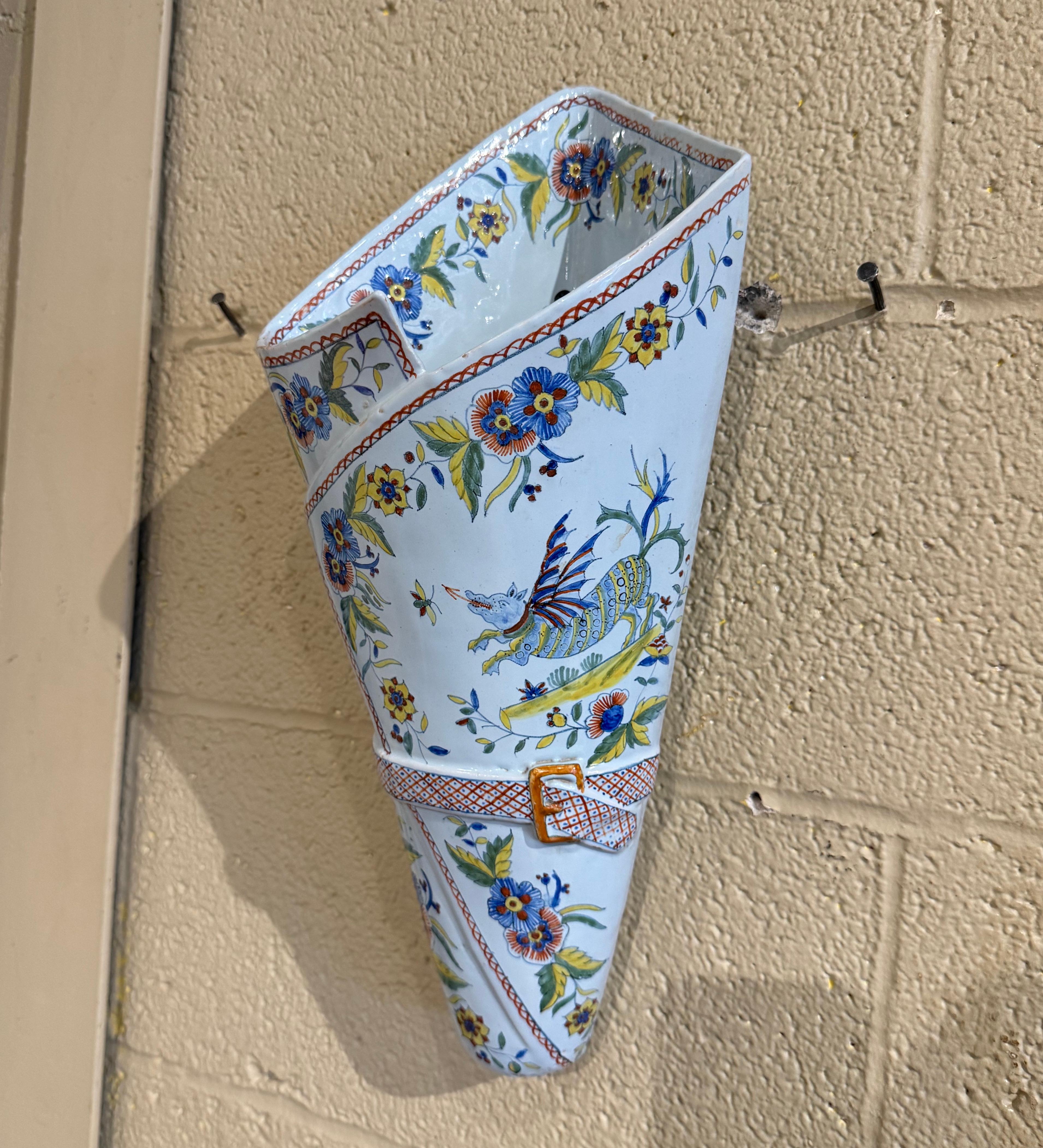 Creado en Bretaña (Francia) hacia 1895, este jarrón de loza artesanal tiene forma de bomba y es cónico, con una hebilla en forma de cinturón en el centro. El gran bouquetiere está decorado con motivos florales y hojas pintados a mano en la paleta de