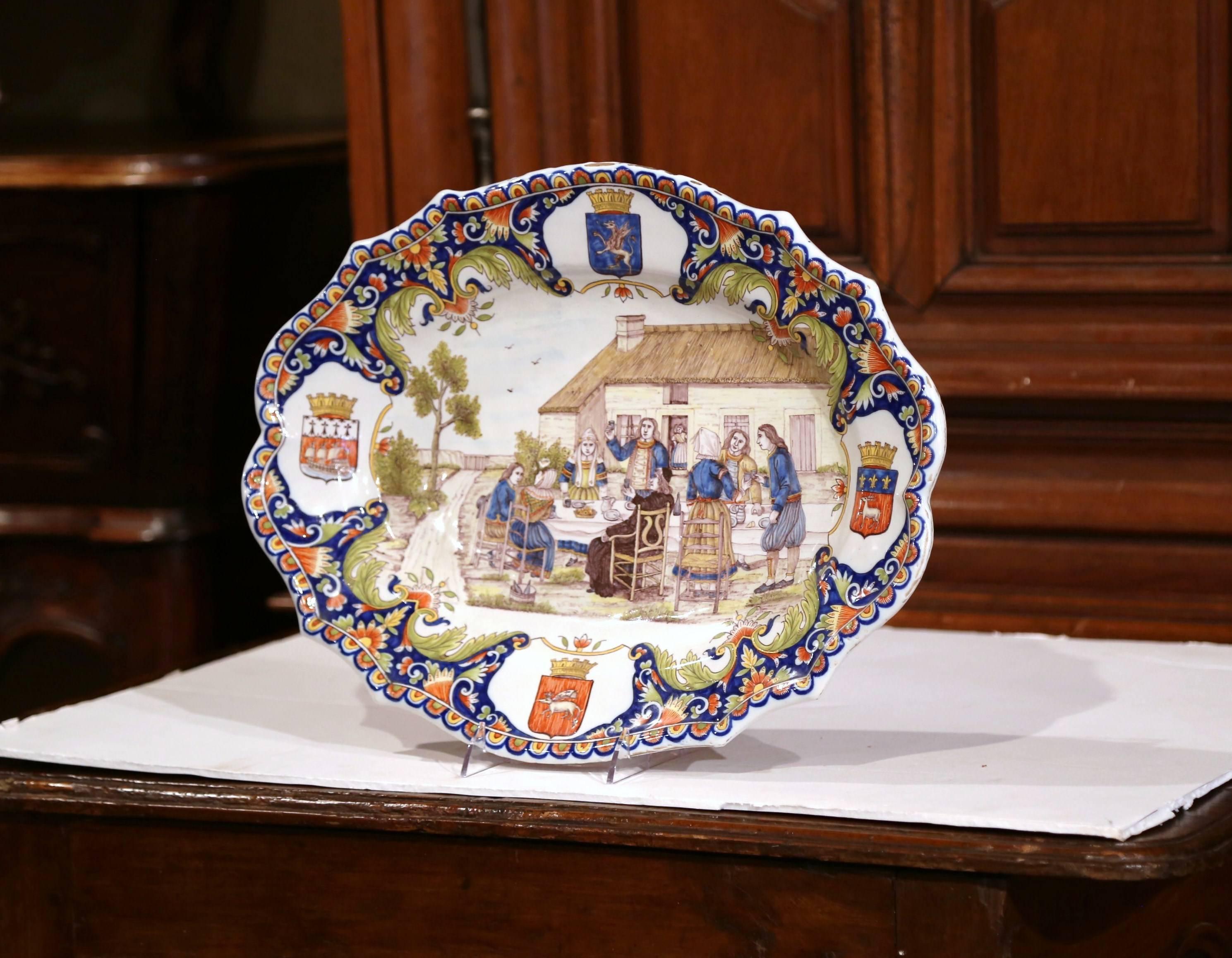 Ce grand plat en céramique a été sculpté en Bretagne, France, vers 1880. L'assiette antique colorée présente une scène de banquet en plein air peinte à la main avec des Bretons qui mangent, boivent et sont vêtus de vêtements traditionnels. Le plat
