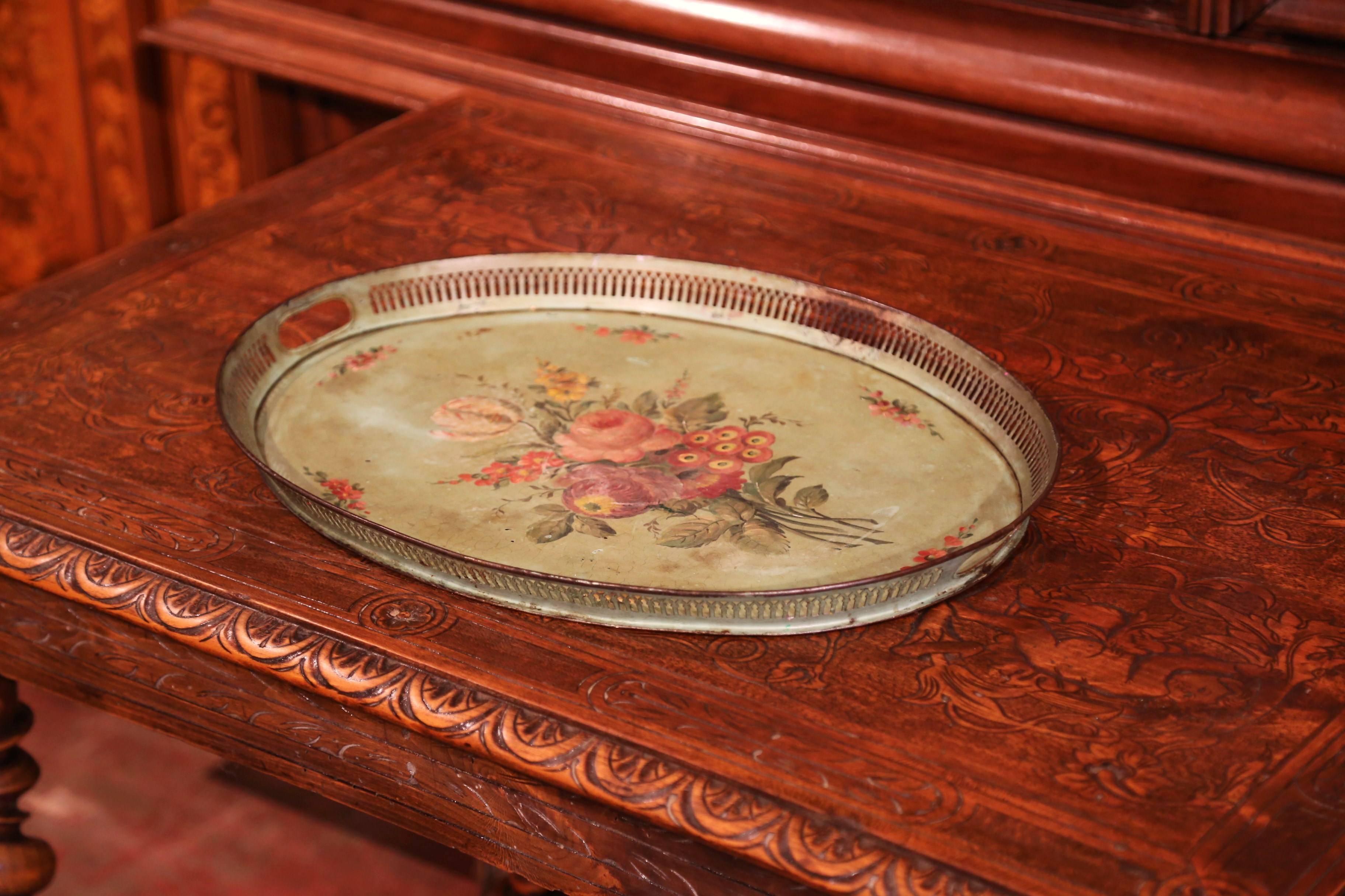 This antique gallery tray was created in Normandy, France, circa 1870; oval in shape, the colorful tray features two handles around the perimeter further embellished by hand painted floral and leaf motifs in the red and orange palette on a light