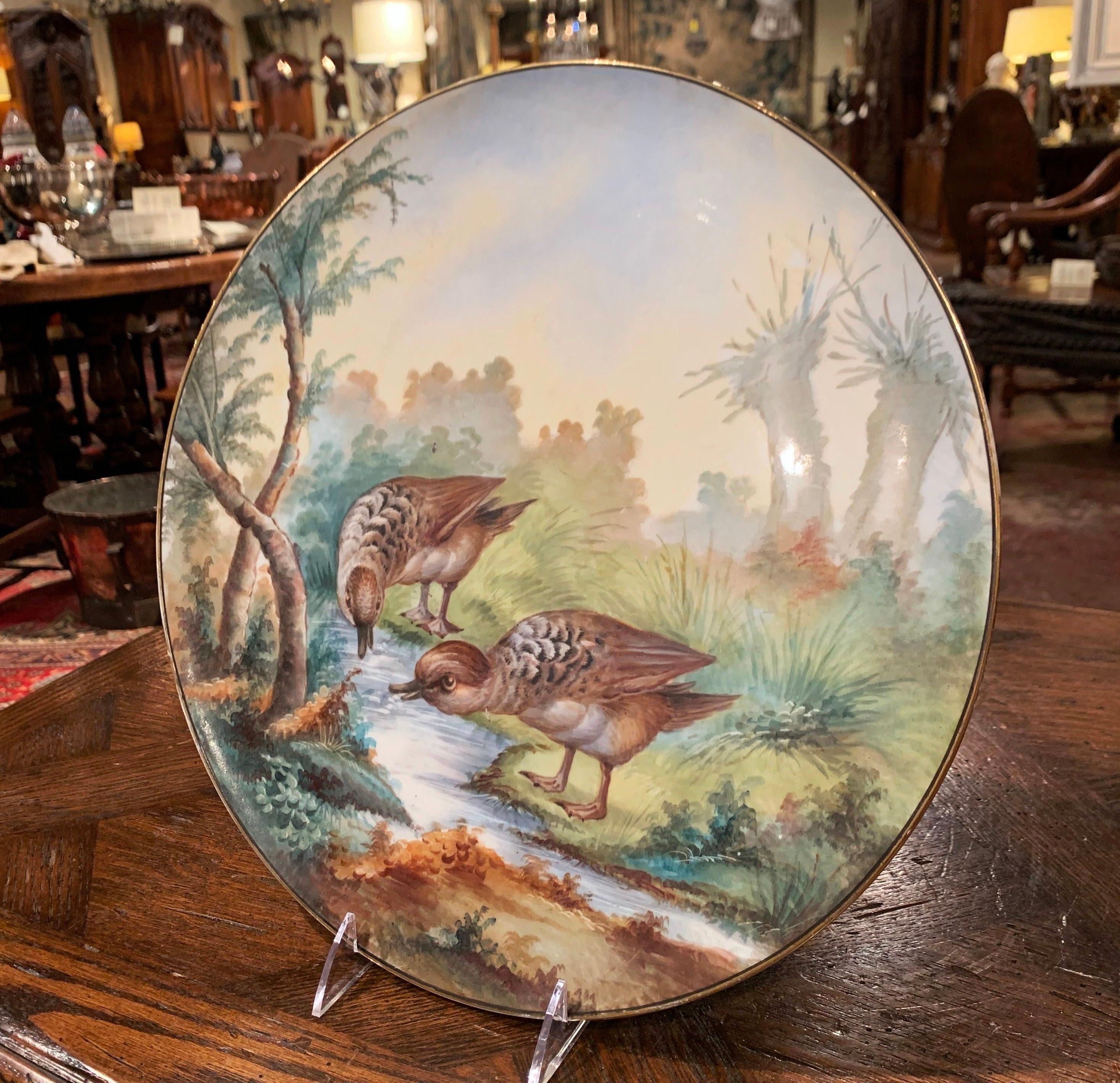 Decorate a wall or a bookcase with this colorful Limoges antique wall platter. Crafted in France circa 1809 and round in shape, the hand painted plate features birds drinking in a river in a luxury landscape; the birds and surrounding scenery are