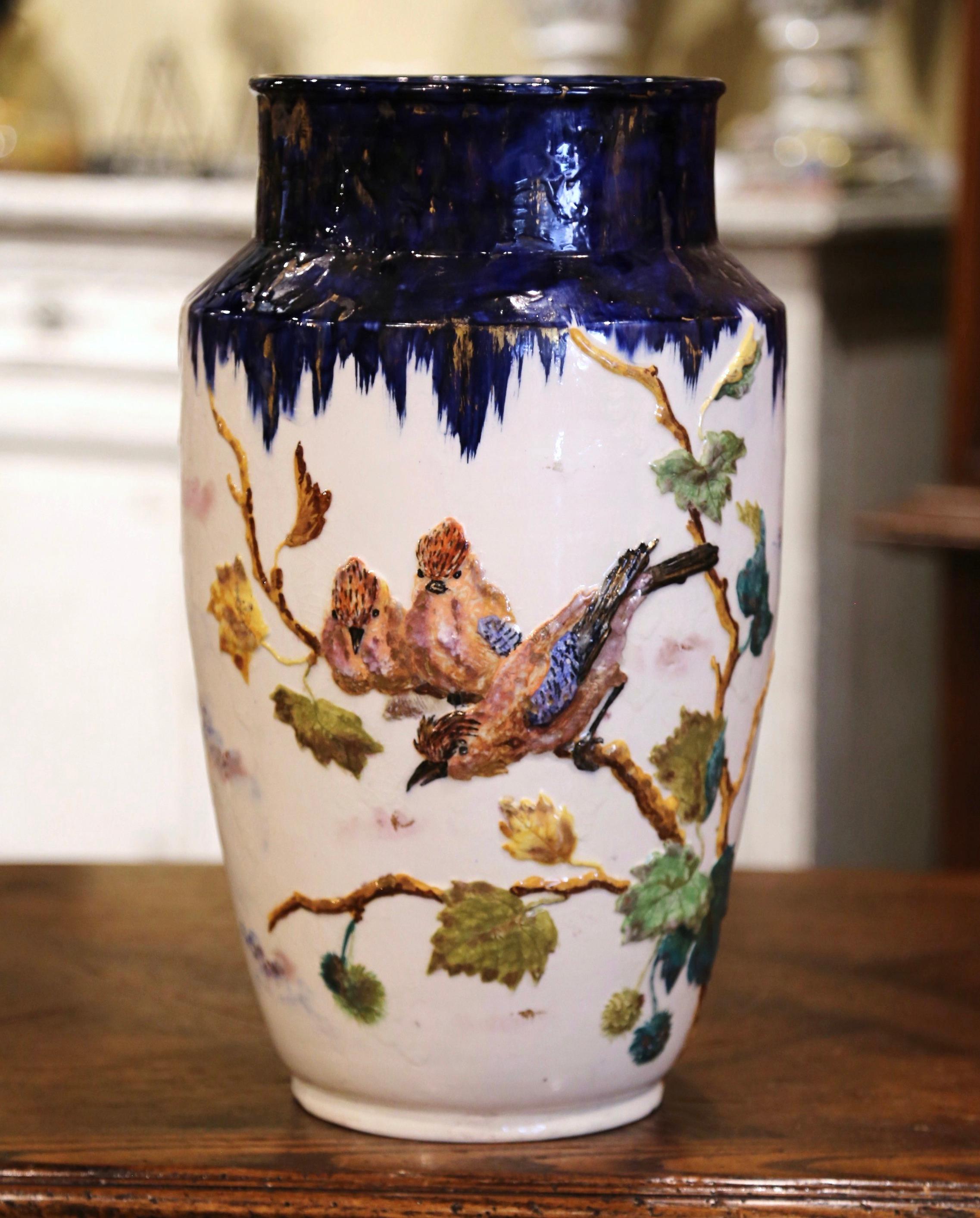 This elegant and colorful antique vase was created in Longchamp, Burgundy, circa 1890, round in shape with high sloping shoulders and body tapered towards the base, the tall ceramic vessel features hand painted bird and foliage motifs in the blue,