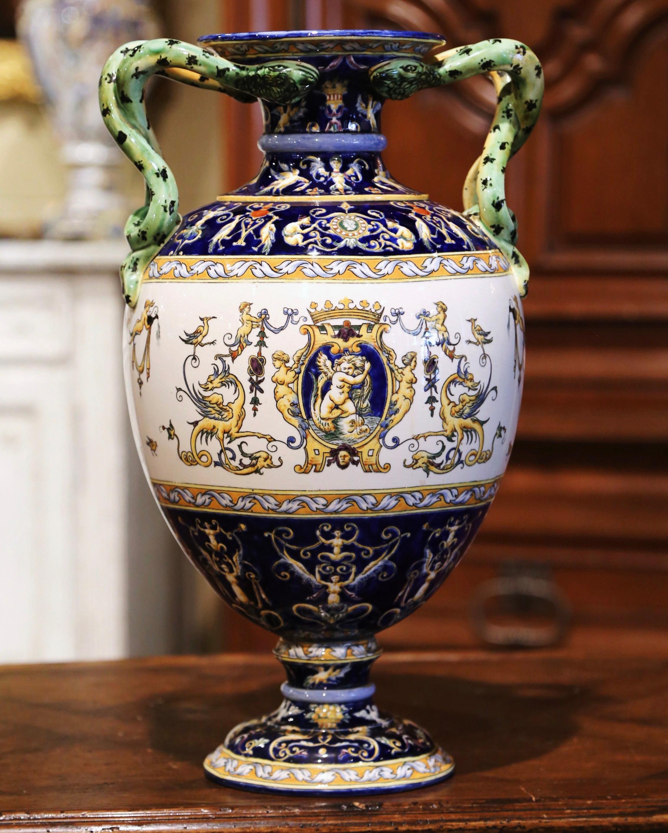 Created in France circa 1890 by the faiencerie de Gien, the antique vase is round in shape and stands on a circular base decorated with bird and leaf motifs. The large vessel features two twisted snake handles over the colorful rim and wide neck.