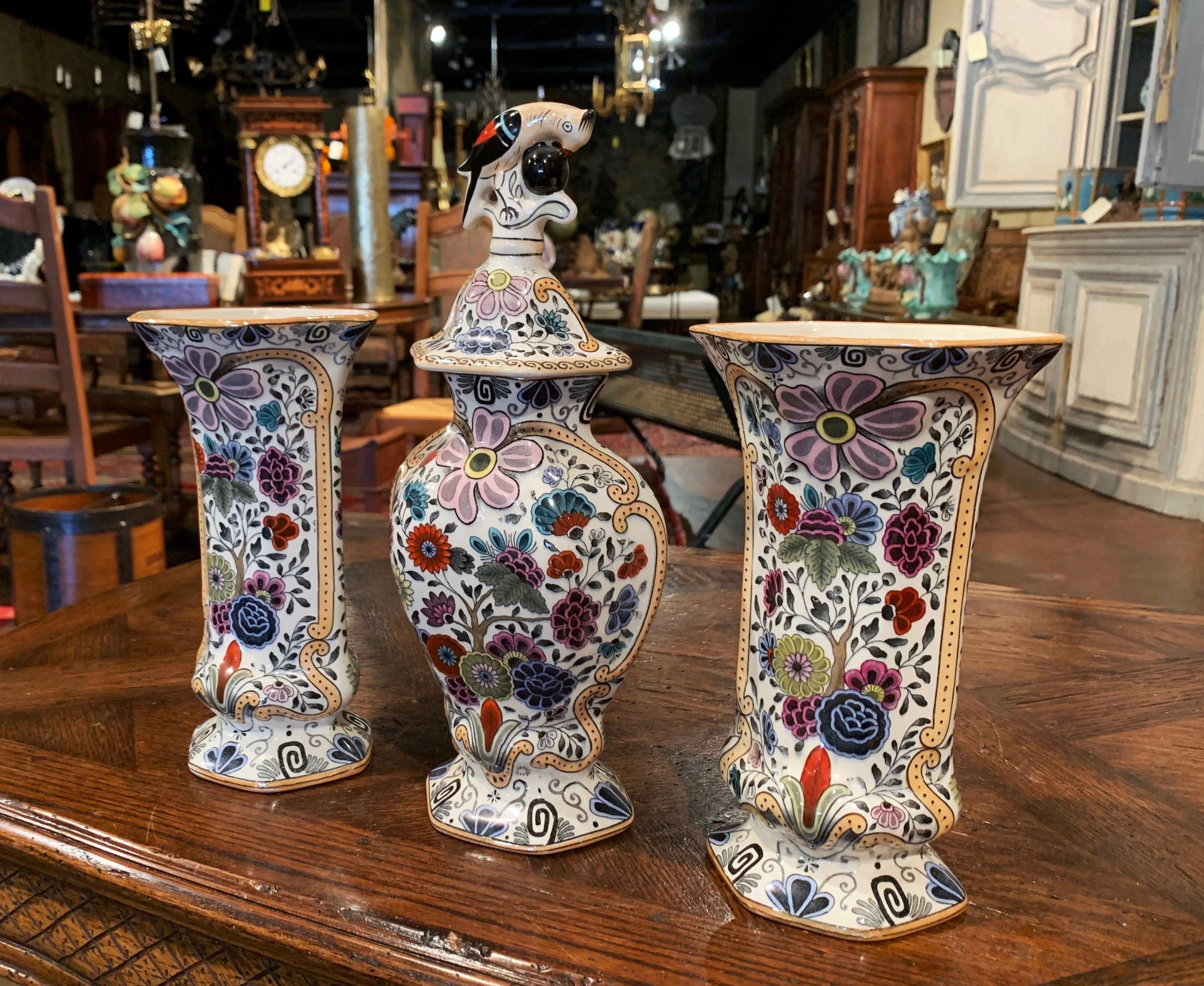 Created in France circa 1890, the three porcelain vases include a pair of trumpet vases and a matching jar with lid decorated with a bird eating a apple in the manner of Delft. All three colorful pieces are hand painted with floral motifs in the