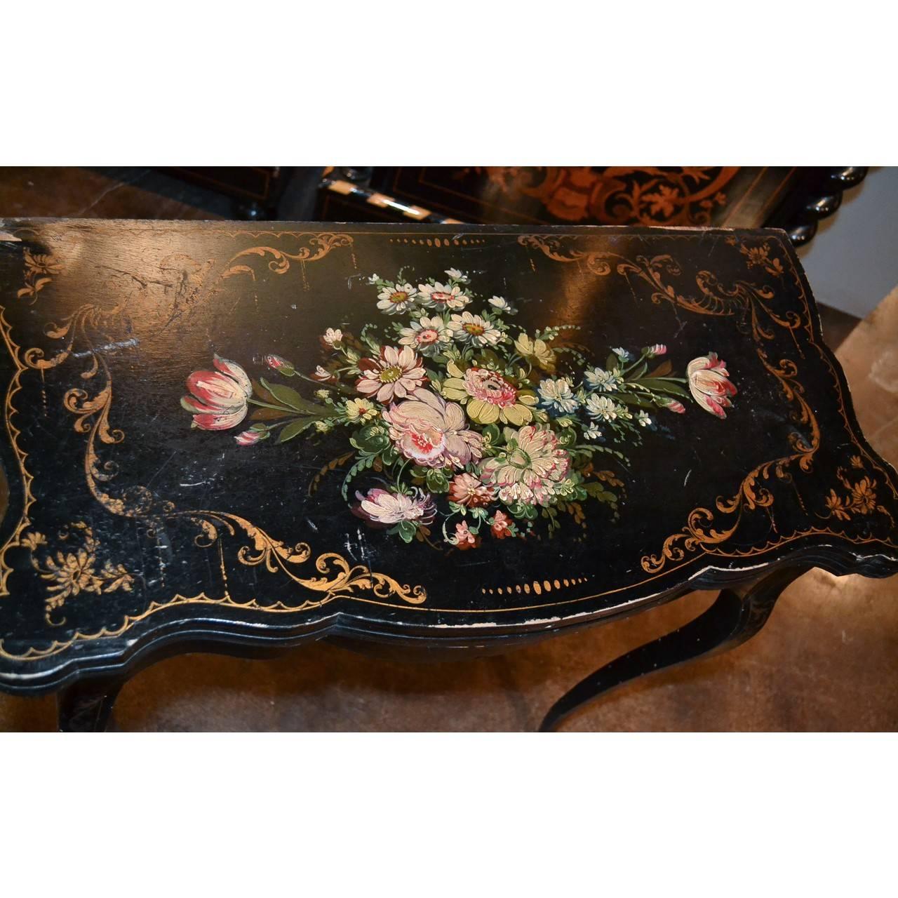 19th century French black lacquered gaming or side table with swivel fold out top and contoured apron. Decorated overall with colorful hand-painted flower clusters and bouquets and accented with gold gilt stylized leaves. The entire on slender and