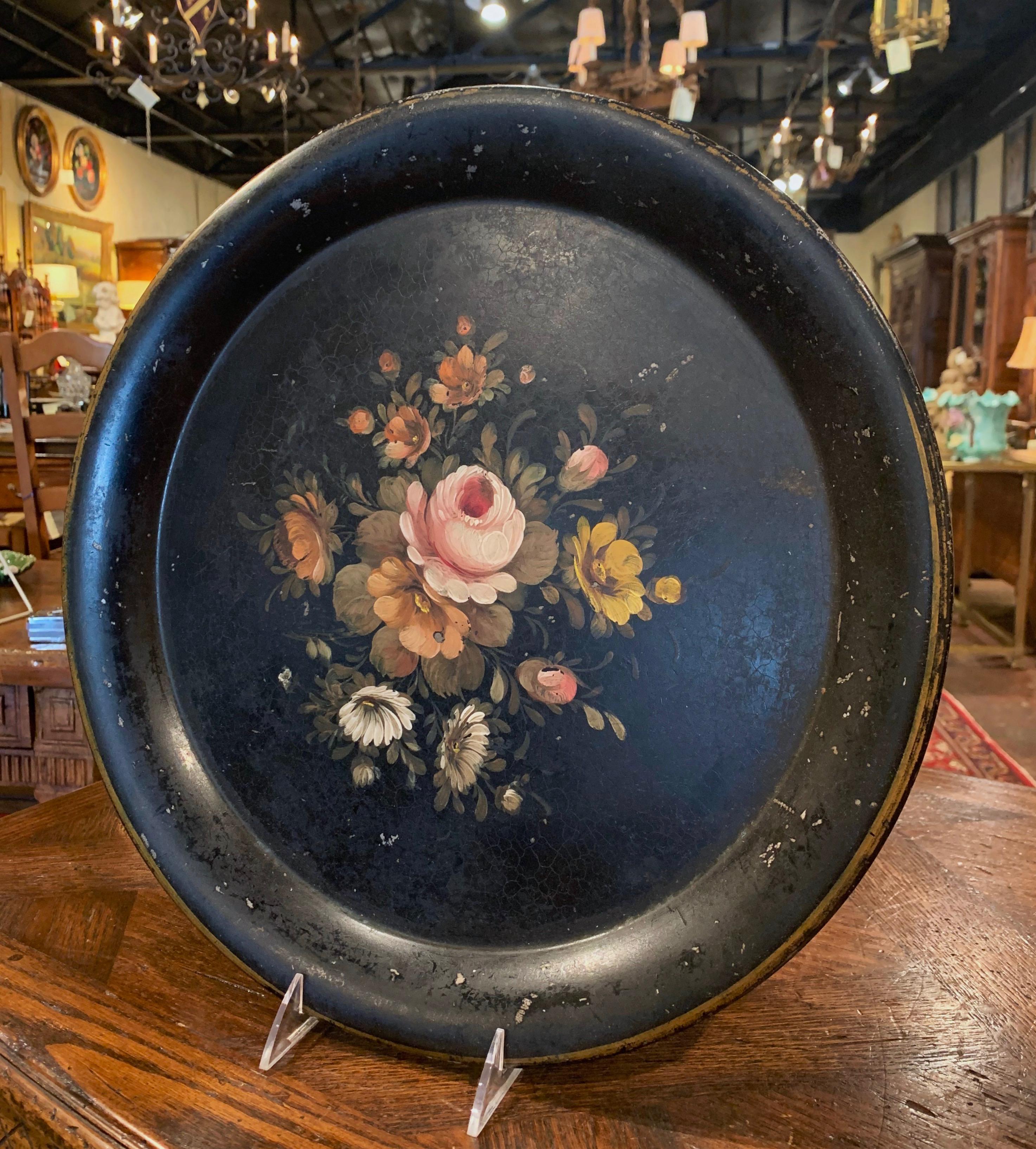 This antique tray was created in Normandy, France, circa 1870; round in shape, the colorful tray features hand painted flowers and leaves in the pink, white and green palette on a black background, embellished with gilt accents around the rim. The