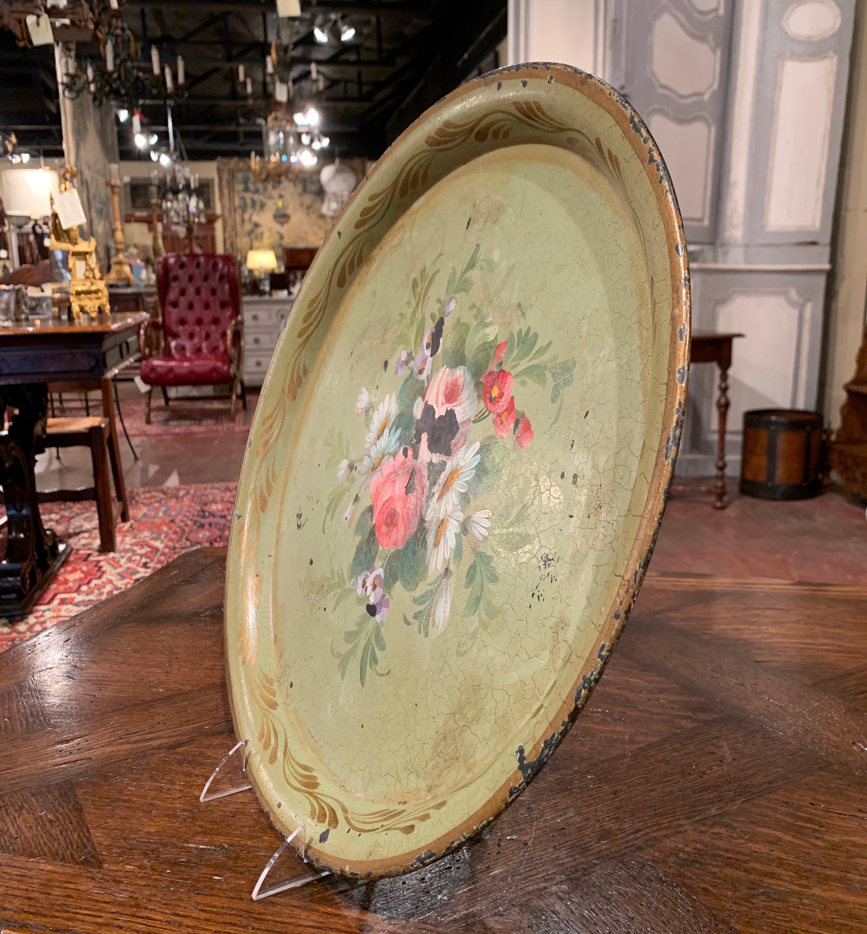 Questo vassoio antico è stato creato in Normandia, Francia, intorno al 1870. Di forma rotonda, il vassoio colorato presenta fiori e foglie dipinti a mano in bianco e rosa su uno sfondo verde chiaro, impreziosito da accenti dorati. Il vassoio è in