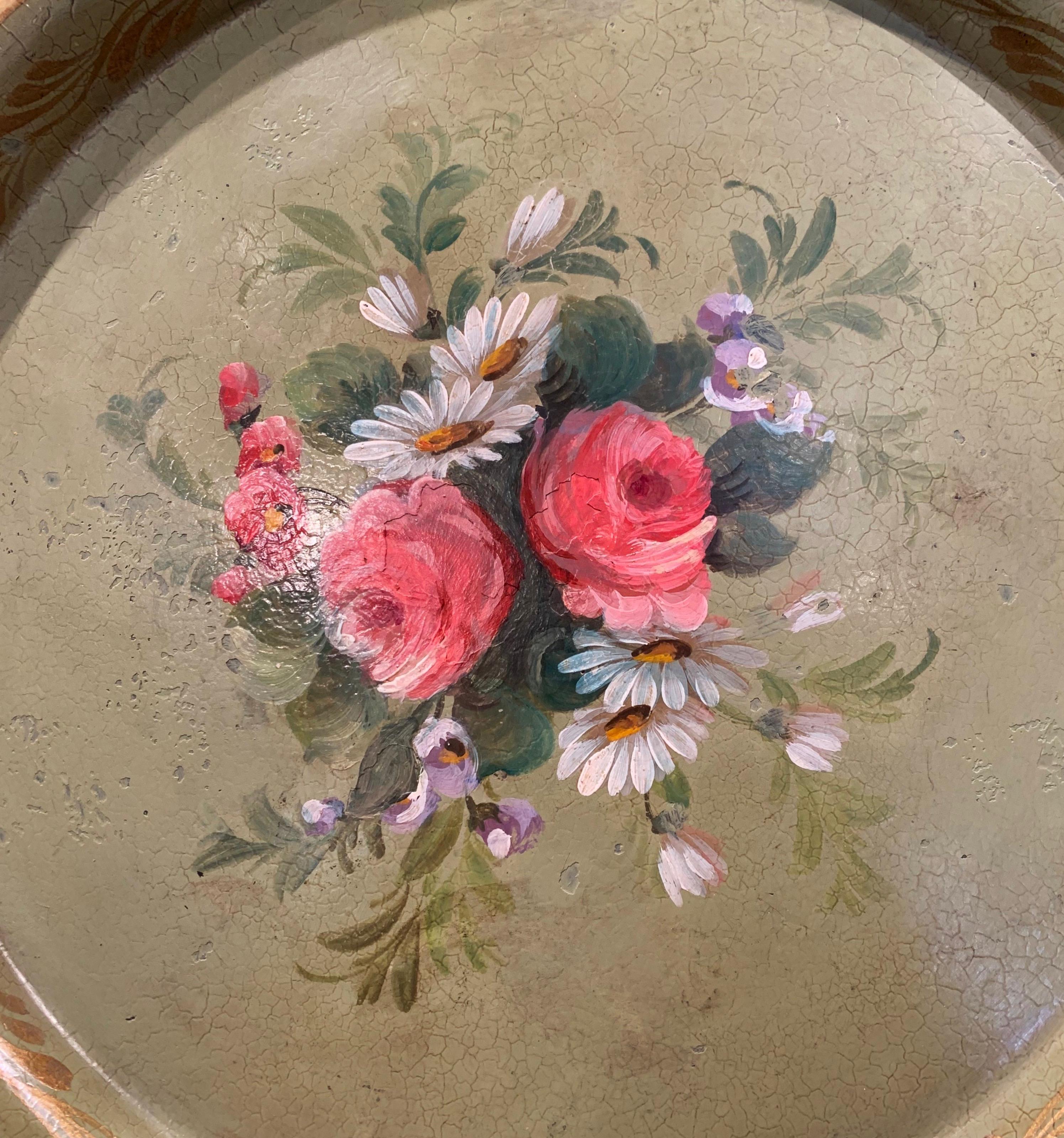 This antique tray was created in Normandy, France, circa 1870, round in shape, the colorful tray features hand painted floral and leaf motifs in the white and pink palette on a light green background, embellished with gilt accents. The tray table is