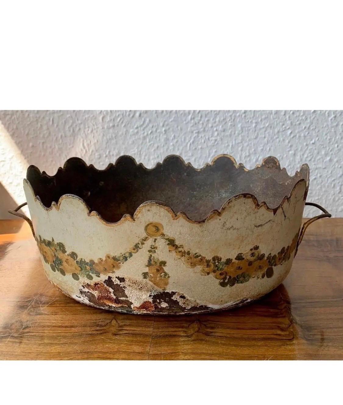 Bellissimo cachepot Jardiniere in toleware europeo con disegni floreali e ghirlande dipinti a mano. 

La fioriera misura 12,5 pollici di larghezza, compresi i manici.