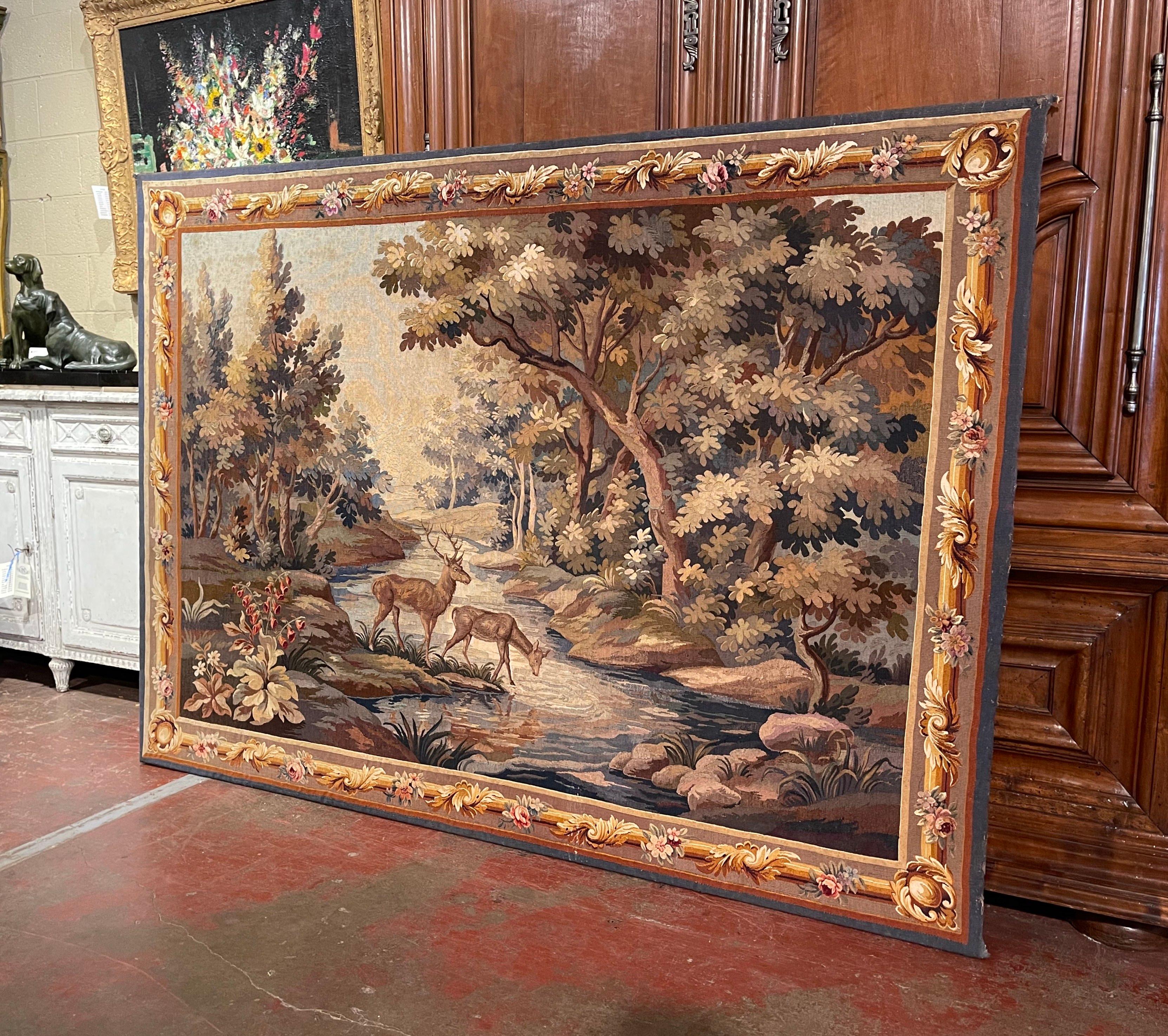 Decorate a ranch or a hunting lodge with this large and colorful antique tapestry. Hand woven in France circa 1870 and secured on a wood stretcher, the verdure tapestry with original border, features a proud buck standing tall, with a doe drinking