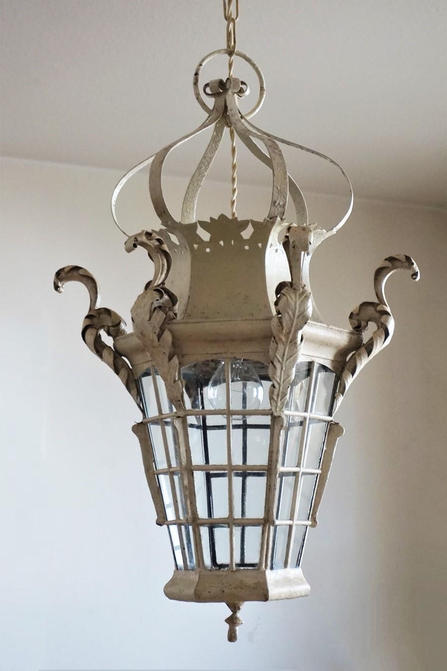 Antique handcrafted wrought iron street lantern with original off-white paint, France, late 19th century. The shaped crown top is leading down to a hexagonal body with glass panels decorated with leaf ornaments, hexagonal glass panel at the bottom.