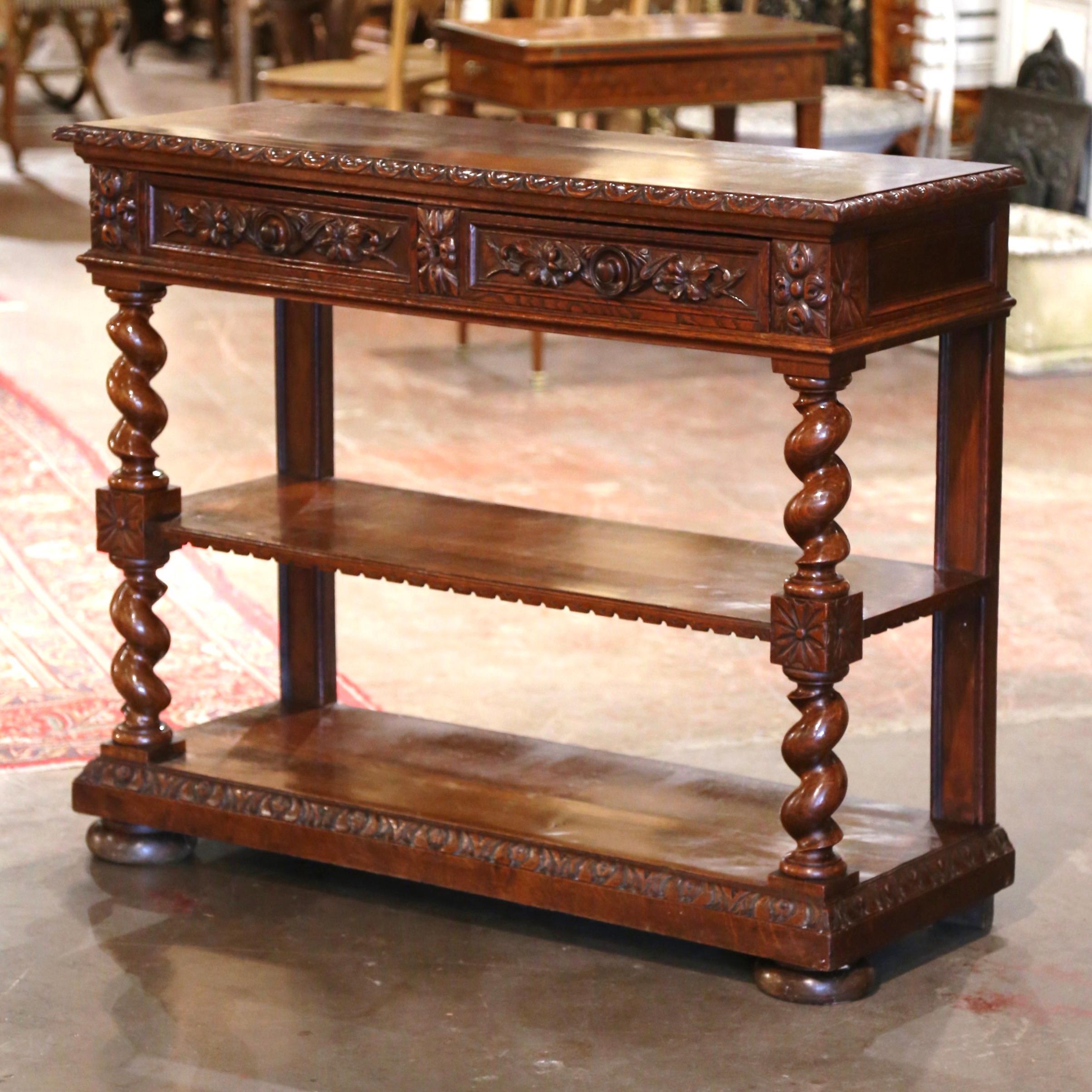 Crafted in France circa 1870, and built of oak wood, the antique console stands on barley twist legs embellished with floral rosette medallions at the shoulders, and ending with bun feet over a decorative plinth base. The desserte surface lifts up