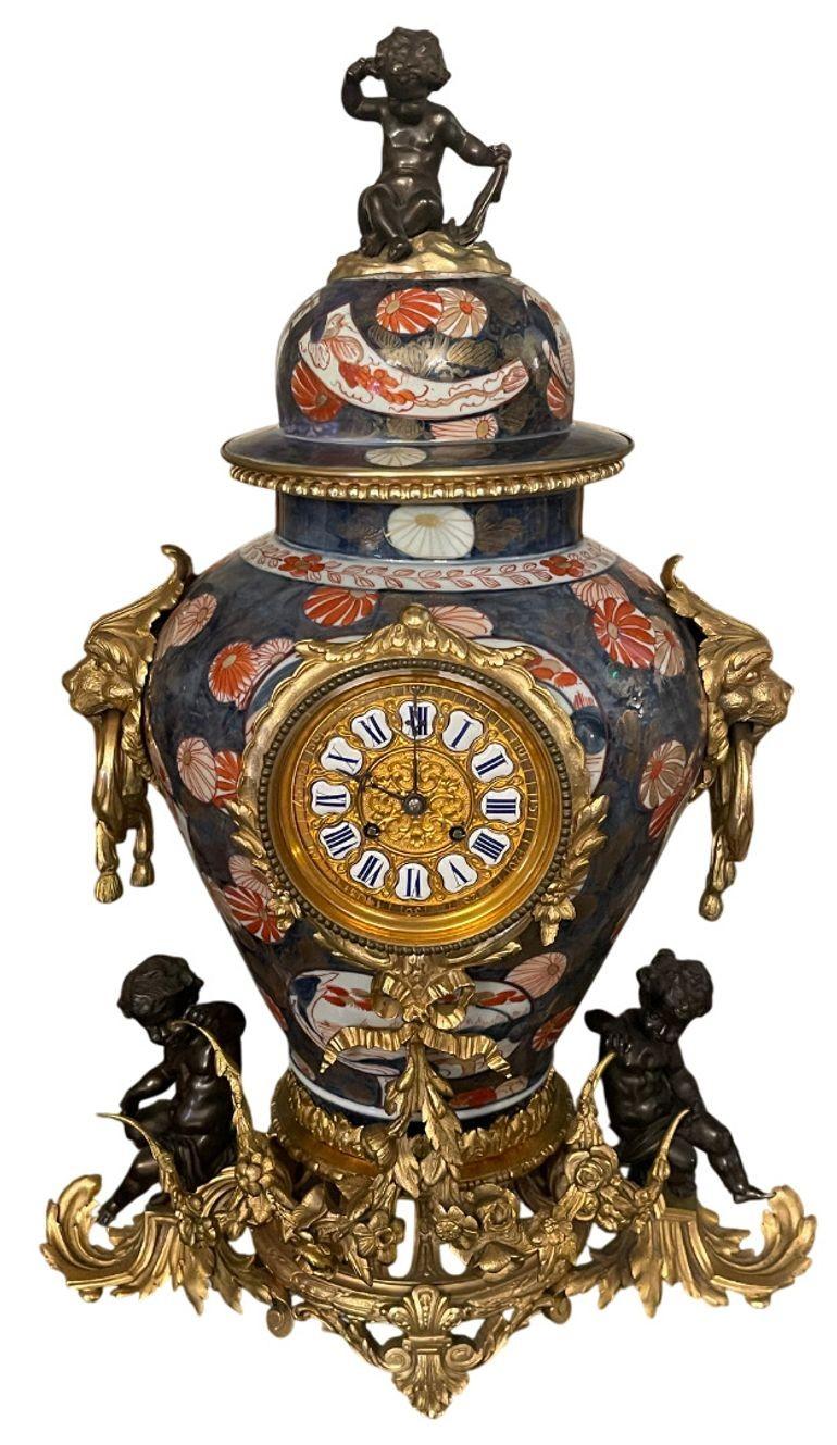 An extraordinary large-scale French Imari porcelain and patinated bronze clock garniture, richly embellished with gilt-bronze mounts. The centerpiece features an enameled circular clock dial inset within a monumental Imari urn, flanked by gilded