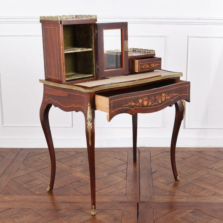 A French 19th century Louis XV style ladies writing desk or ‘bonheur du jour’ having a drawer beneath the leather writing surface and an upper superstructure with beveled glass cabinet to the left and small upper right-hand drawer. The piece is