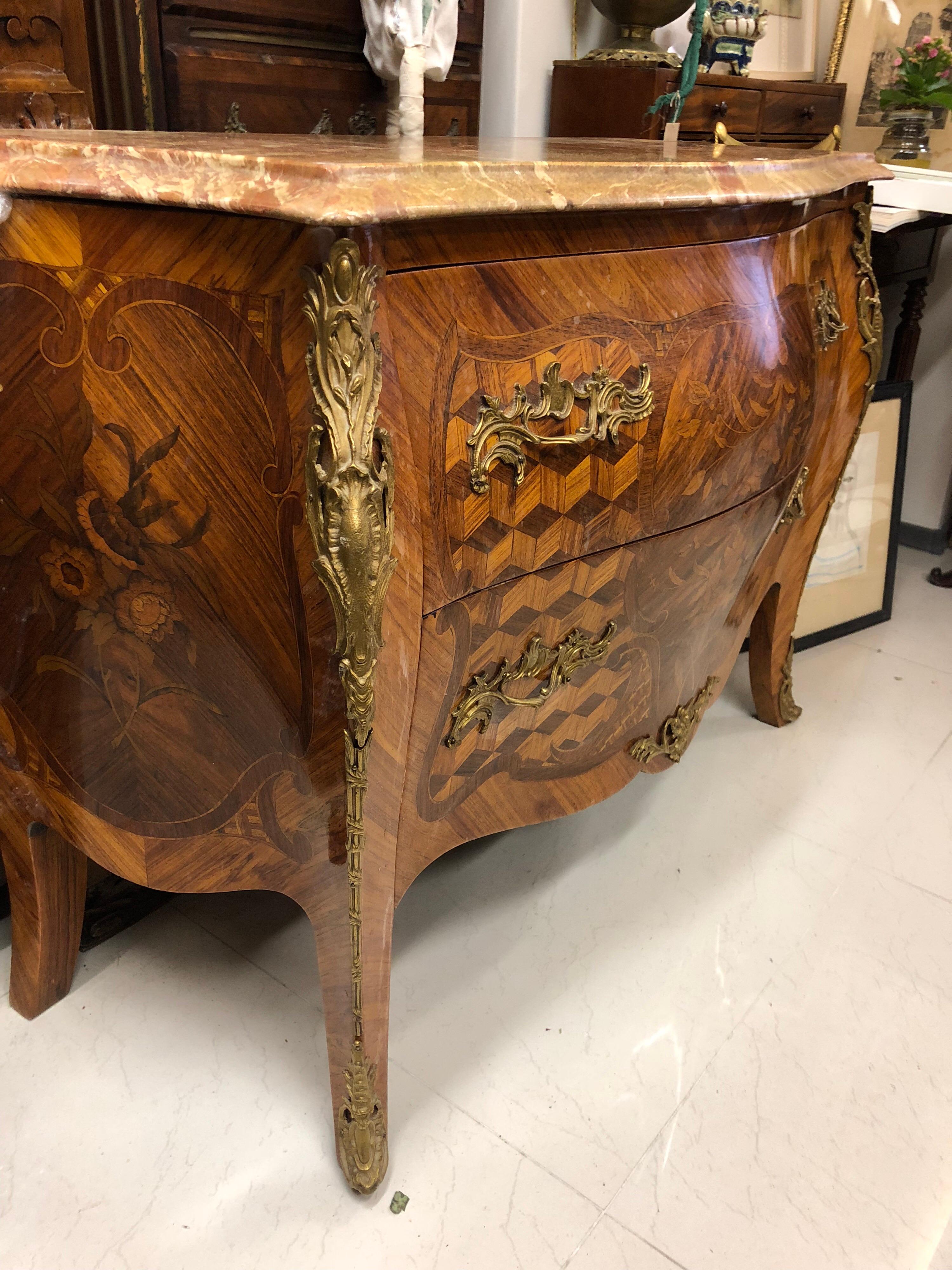 French two drawers bombe commode with curved front and sides in rosewood veneer and violet wood with inlaid decoration of flowering branches and bottomless cubes. Ornamentation of Rococo bronzes. Marble top with veined red breccia. Louis XV style.