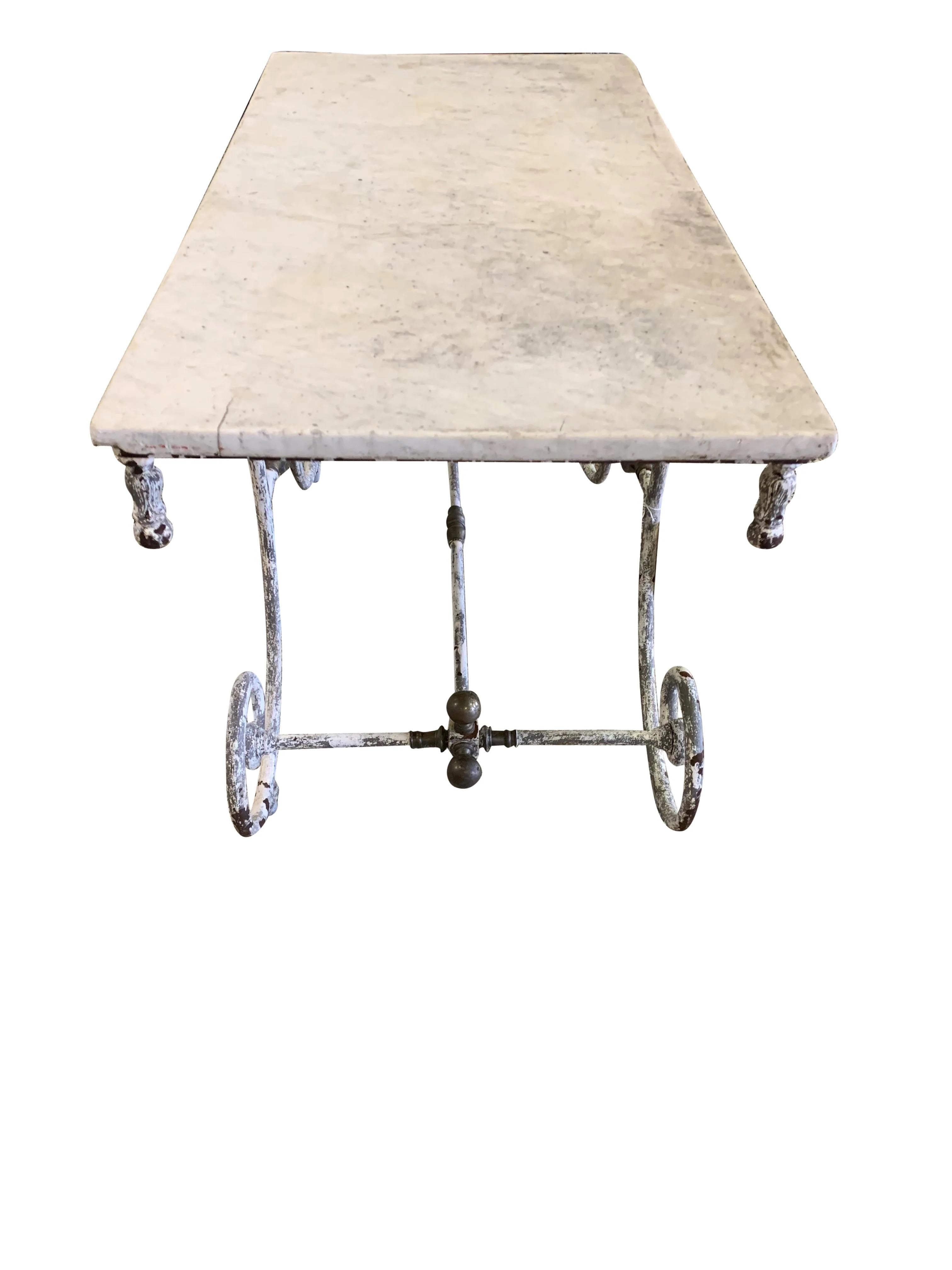 A gorgeous 19th century French marble top pastry table featuring old white painted patina on the iron base. This beauty features decorative brass hardware with patina and a white veined marble top. Ideal for use as a kitchen island or could also