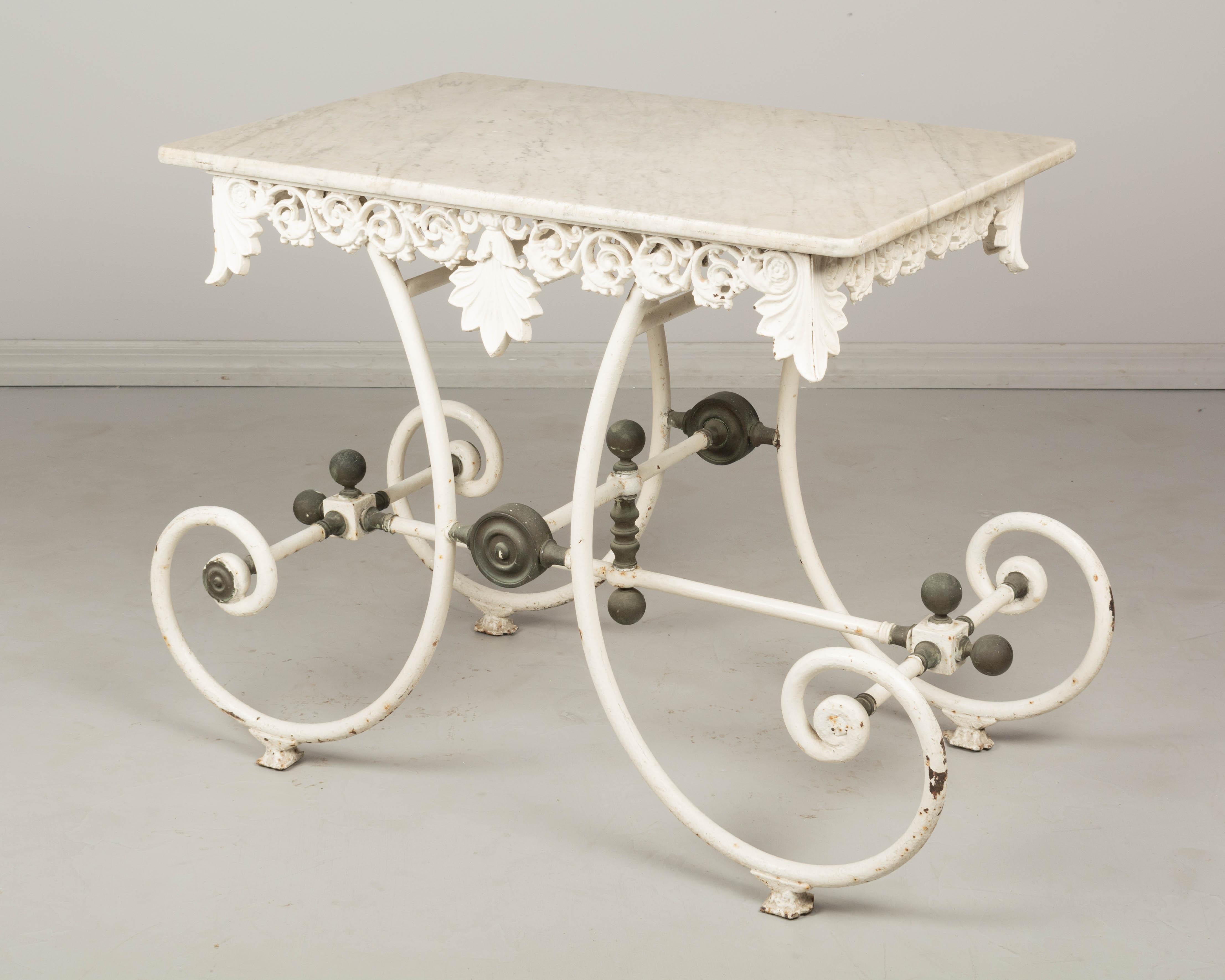 A 19th century French marble top pastry table with old white painted patina. Curved wrought iron base. Decorative brass hardware with grey patina. Ornate cast iron frieze around the perimeter with large acanthus leaves. White veined marble top.