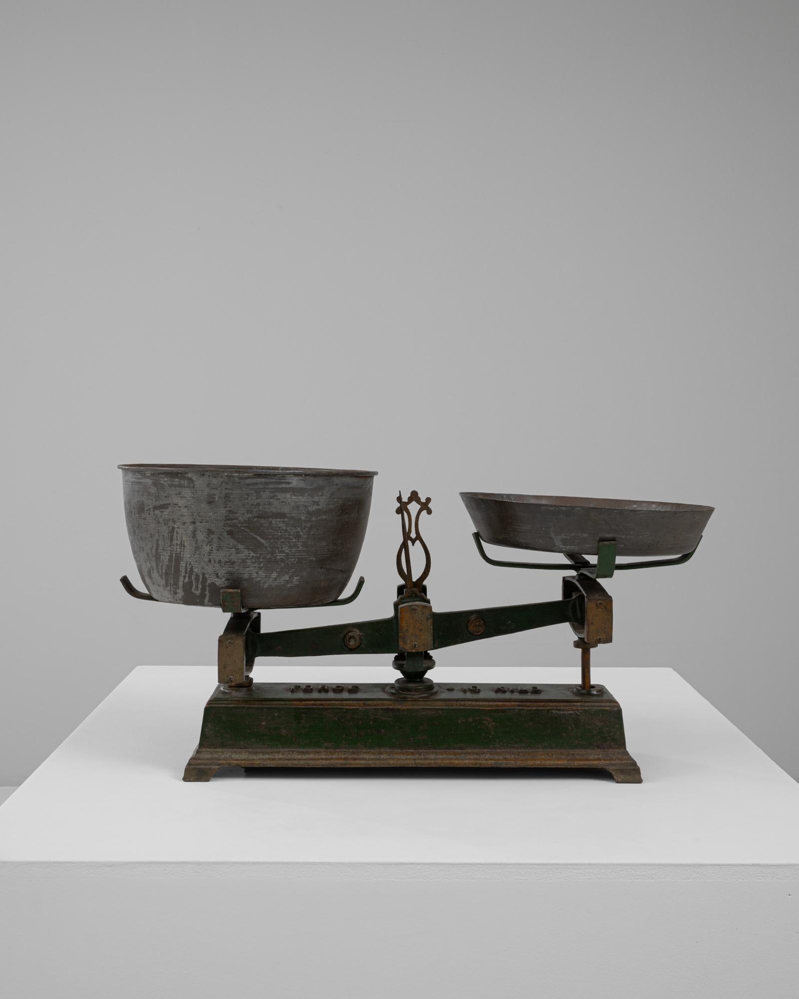 Questa bilancia francese in ferro e metallo del XIX secolo unisce l'artigianato utilitario a un caratteristico carattere invecchiato. La base in ghisa, rifinita con la sua vernice originale verde intenso con sfumature dorate, offre una patina ricca