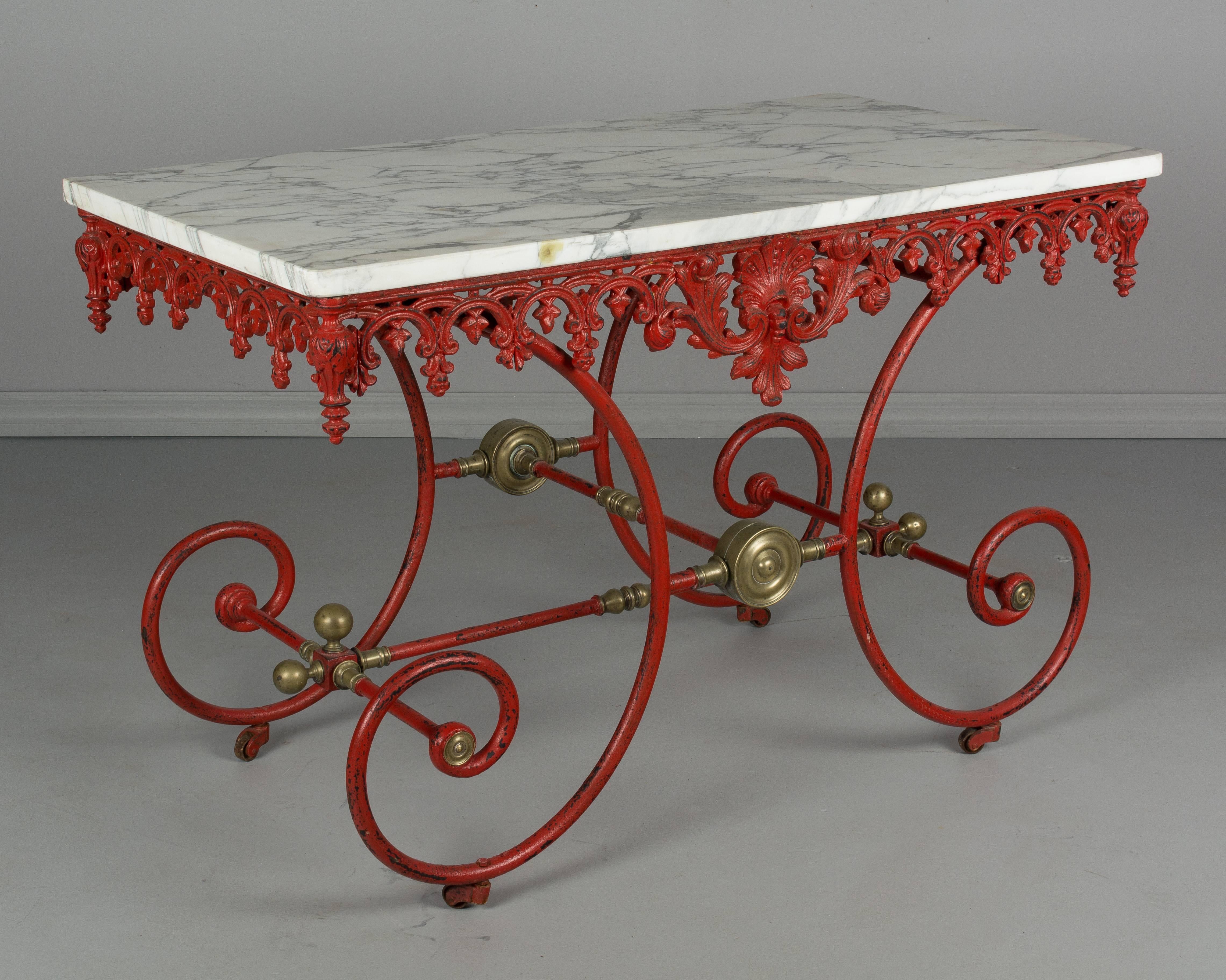 A 19th century French pastry table with original brilliant red painted patina. Curved wrought iron base with decorative brass hardware. Ornate cast iron frieze around the perimeter with large acanthus leaves and finials at each corner. Original