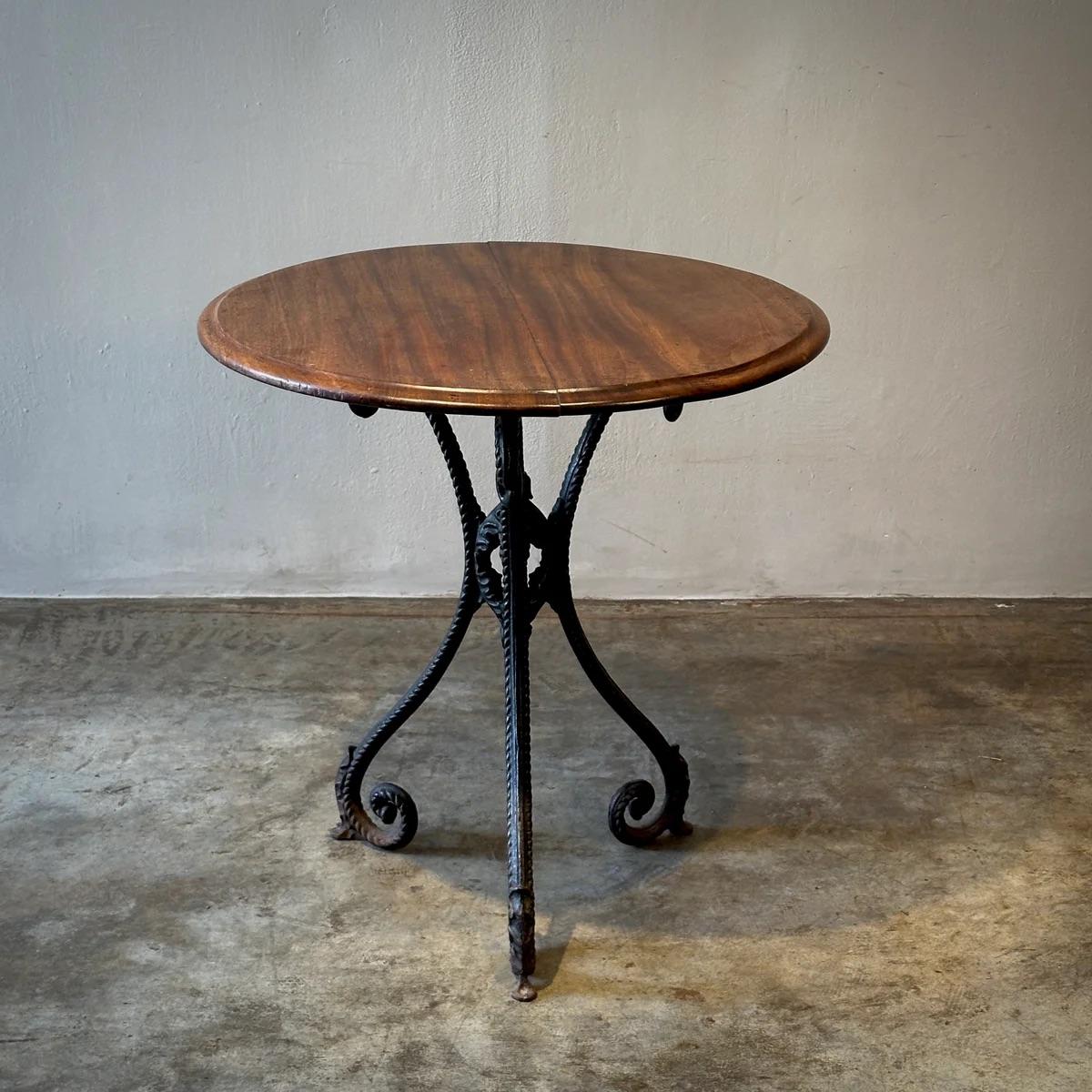 Evoquant la haute société des cafés parisiens, cette table décorative avec base en fonte et plateau en acajou allie délicatesse et solidité. La base, inspirée des débuts de l'Art nouveau, présente des détails de corde complexes et d'élégants motifs