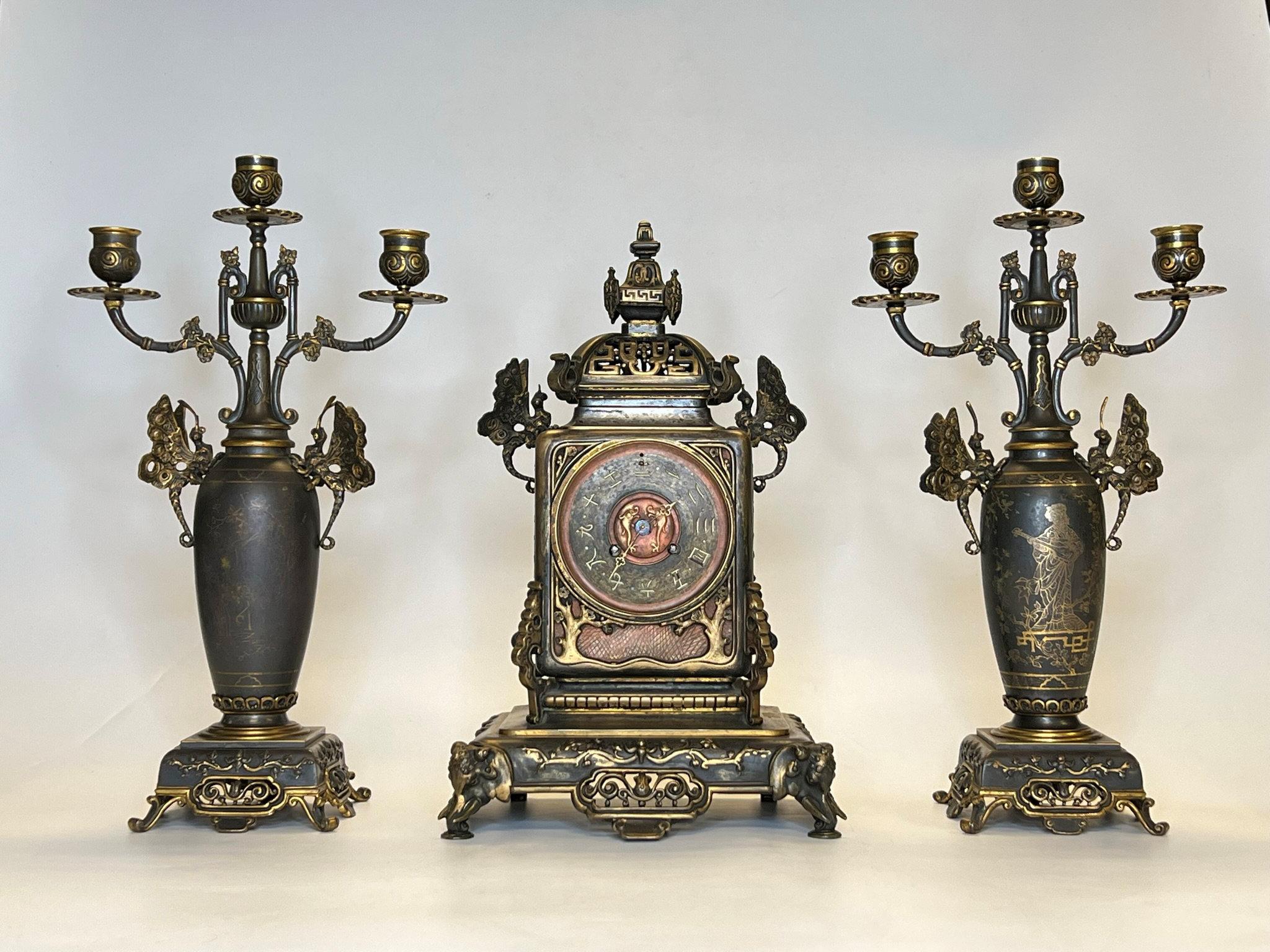 19th century French mantel clock and matching candelabra set in the Japonisme style similar to those from Christofle, with dragonflies at the shoulder of each, and each with damascened inlaid gold cartouches including maidens, herons, butterflies