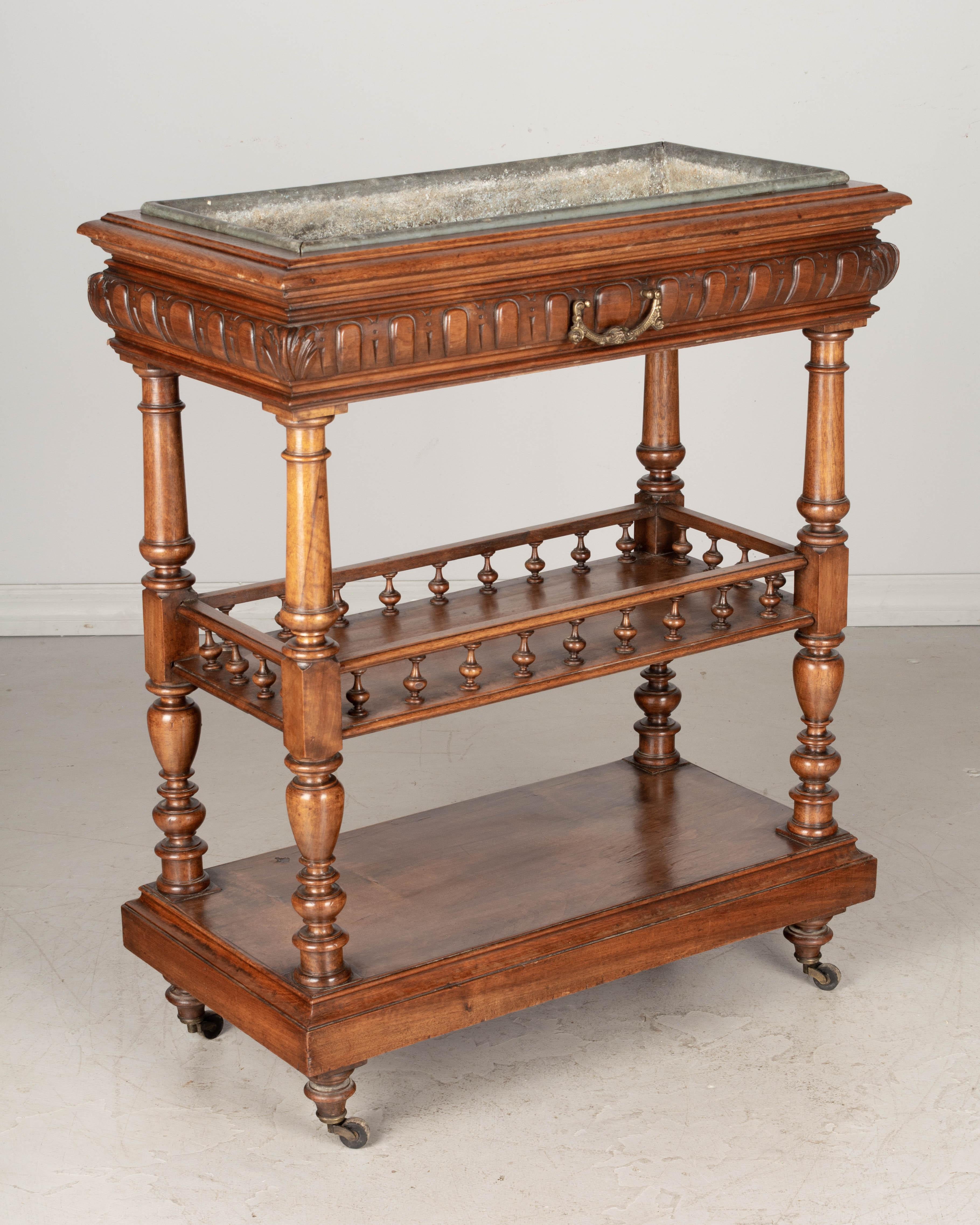 A 19th century French jardinière, or plant stand made of solid and veneer of walnut with removable zinc tray. Middle shelf has a gallery with turned spindles. Castors roll smoothly. Waxed patina. All original. Minor loss of veneer on bottom shelf.