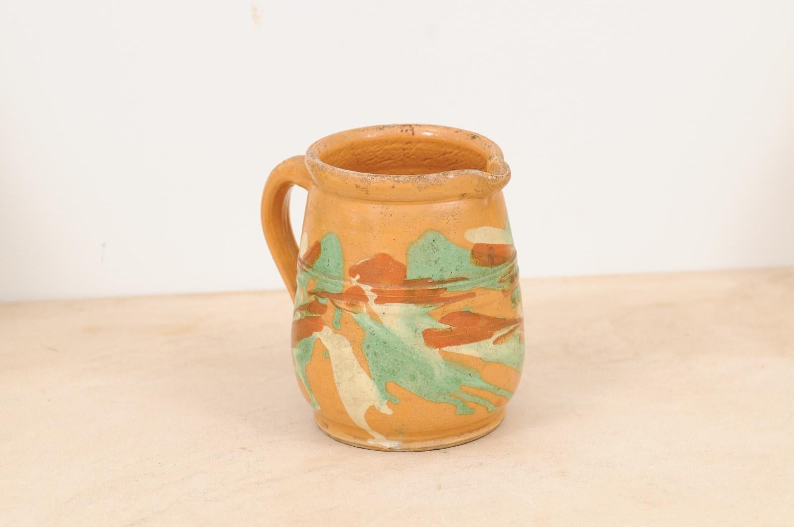 A French jaspe pottery pitcher from the 19th century, with yellow glaze and green accents. Created in France during the 19th century, this jaspe pottery pitcher features a yellow glaze accented with green, cream and brown motifs. Showcasing a back