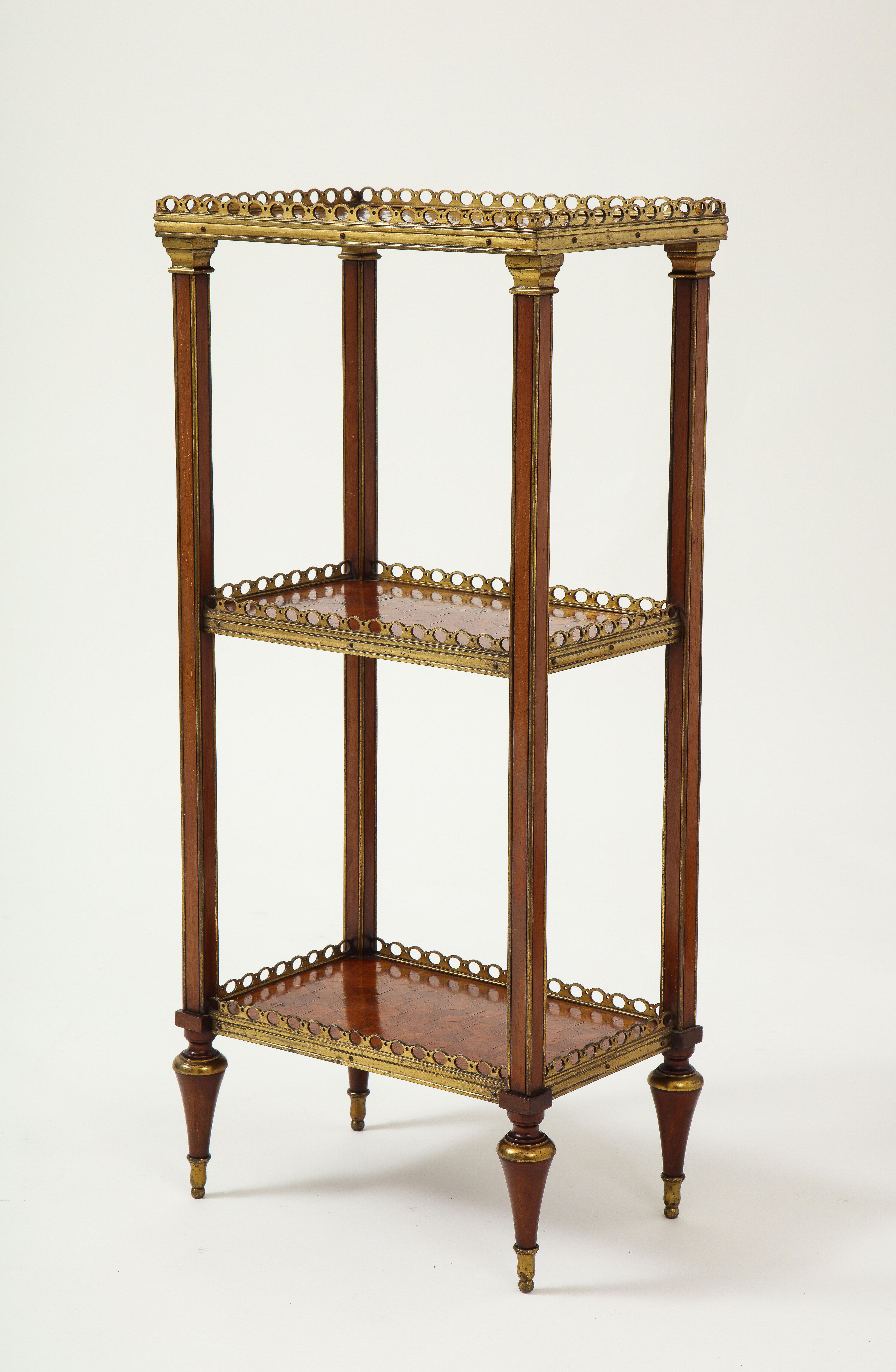 Elegant proportions and easily movable around a room. With three tiers, each with geometric parquetry inlay and gilt metal galleried top; raised on metal trimmed-square tapering uprights headed by gilt metal capitals on toupie feet.

  
