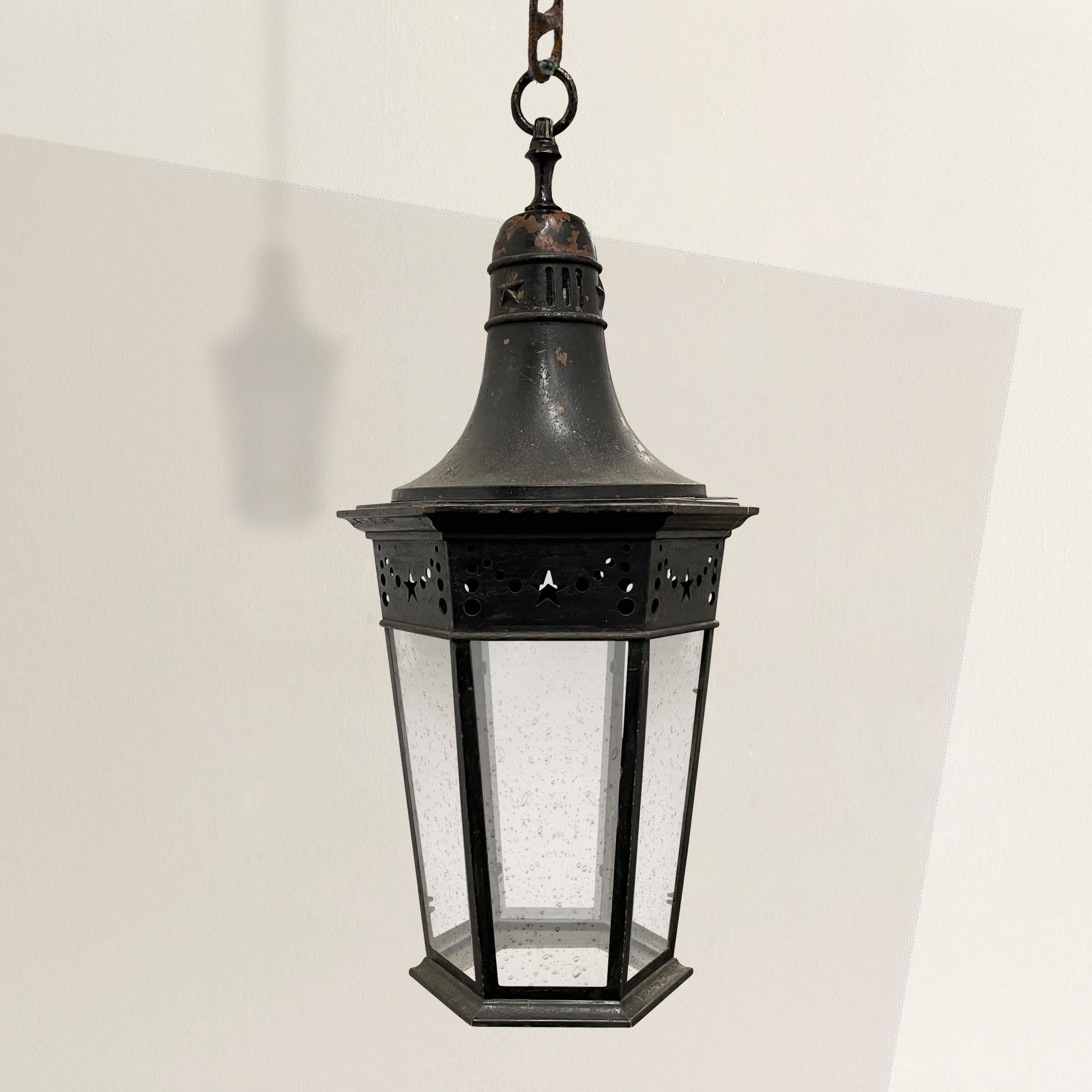 A charismatic and full-of-personality 19th century French black painted copper gas lantern, now electrified, with six tapered sides with a pierced stylized swags with stars and graduated dots on the frieze of each side, and with new seeded glass