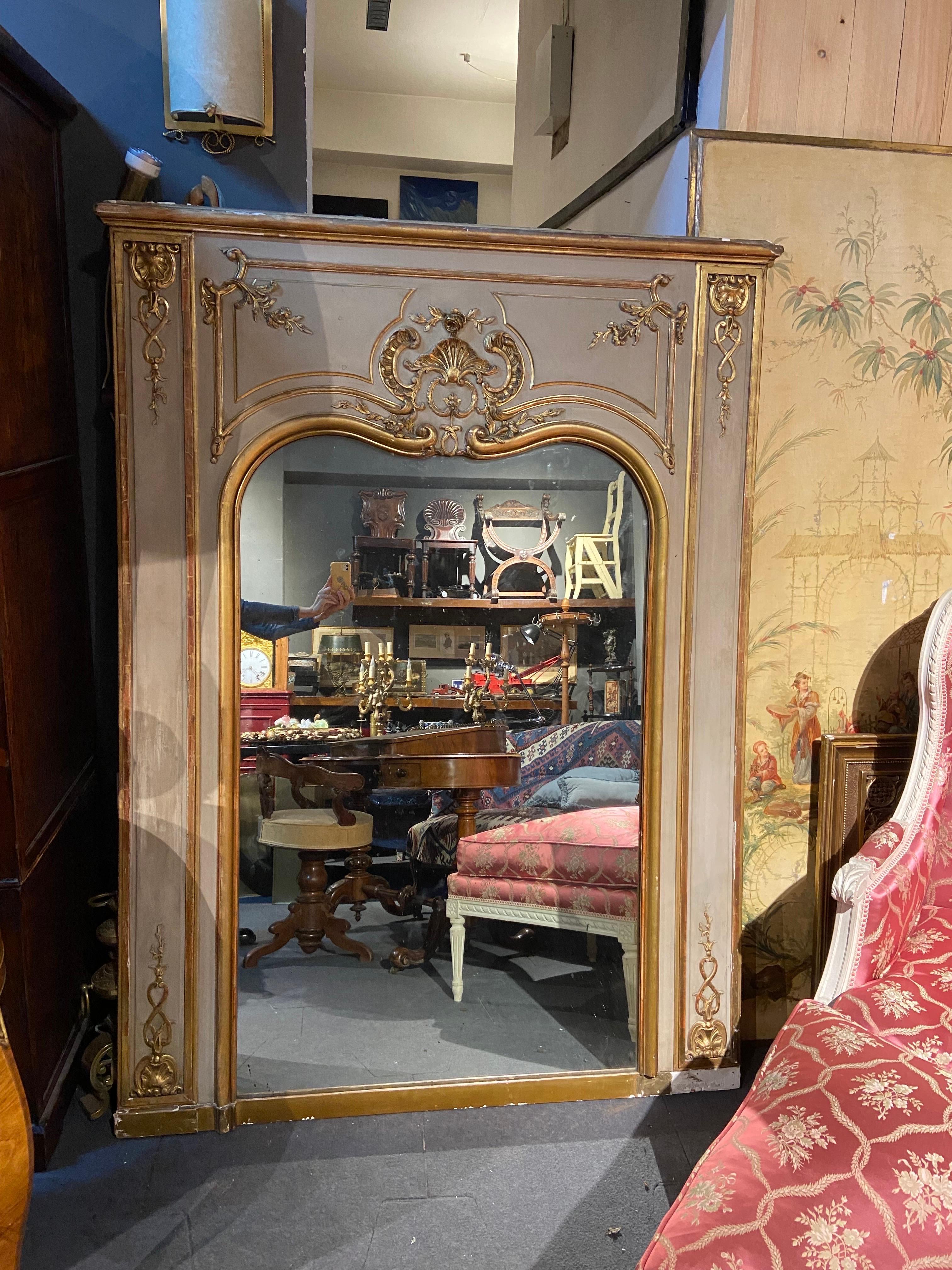 Grande specchio francese in legno dorato intagliato a mano e ben dipinto di colore grigio chiaro vicino al verde chiaro.
Bellissimo esempio di gusto ottocentesco con ornamento centrale e delicate decorazioni sui lati.
Condizioni autentiche molto