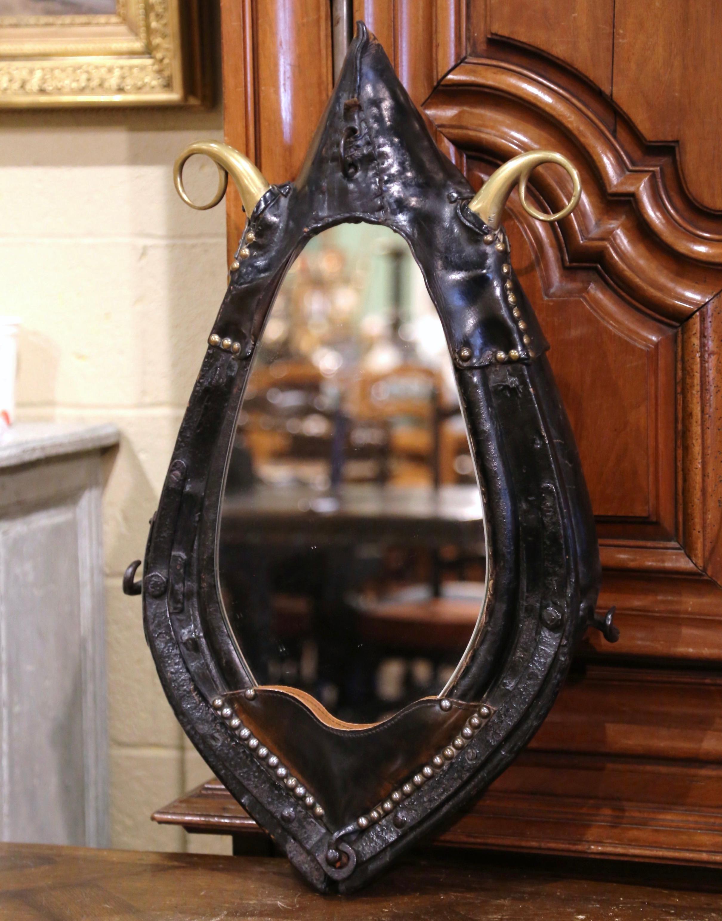The wall hanging mirror is a unique find for a ranch home or hunting lodge. The mirror is framed by a fine, antique horse collar from France, circa 1880. The collar is carved in wood and covered with leather and original iron and bronze hooks. This