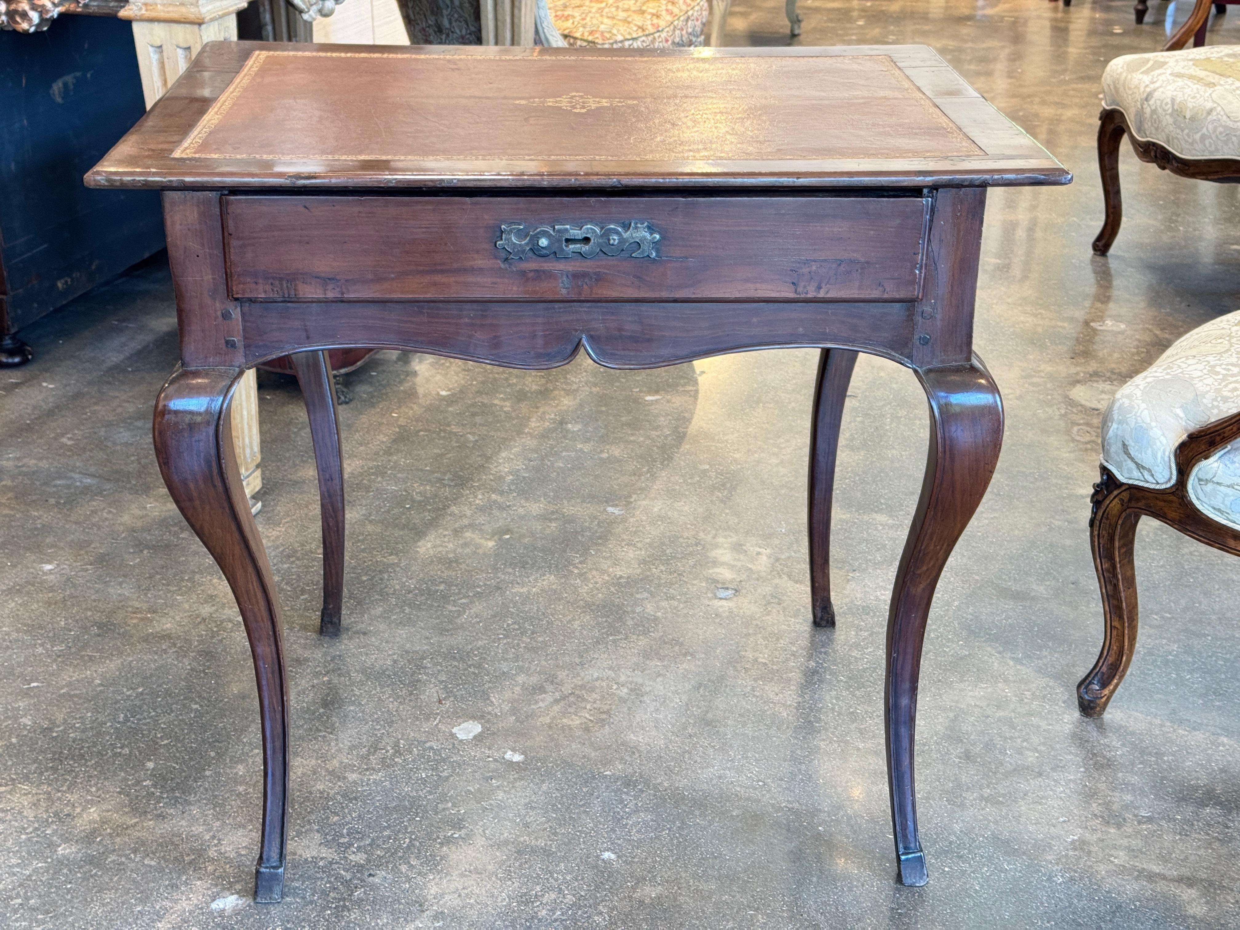 Table à écrire française du XIXe siècle, avec un plateau en cuir estampé, une bordure à la feuille d'or et un médaillon central. La table repose sur de gracieux pieds cabriole et comprend un seul tiroir avec un écusson en laiton d'origine. Le