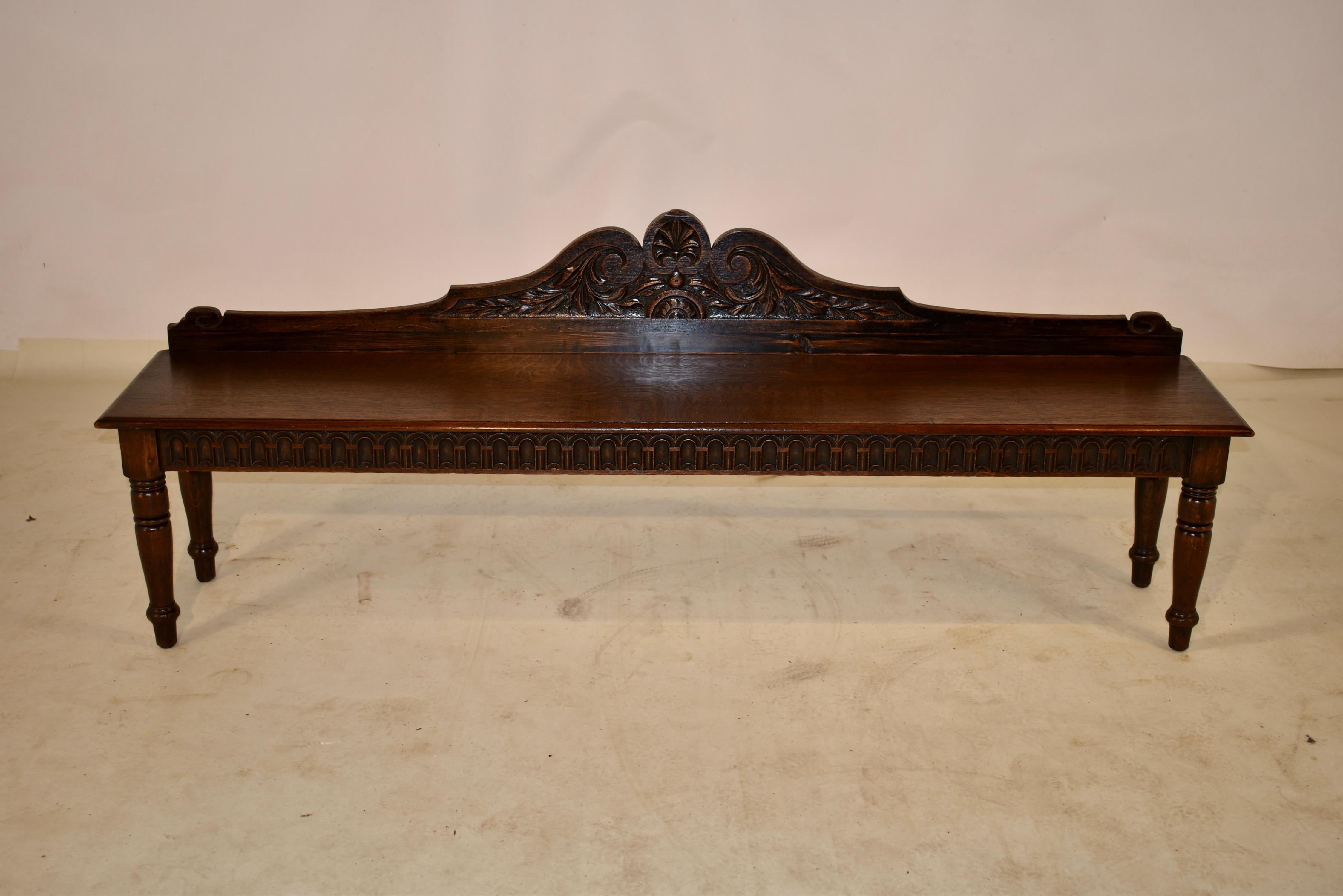 19th century oak long window seat from France. The back is hand scalloped and carved over a seat which is made from a single board. The apron is also hand carved in a nulling pattern and the bench is supported on hand turned legs. This is a lovely