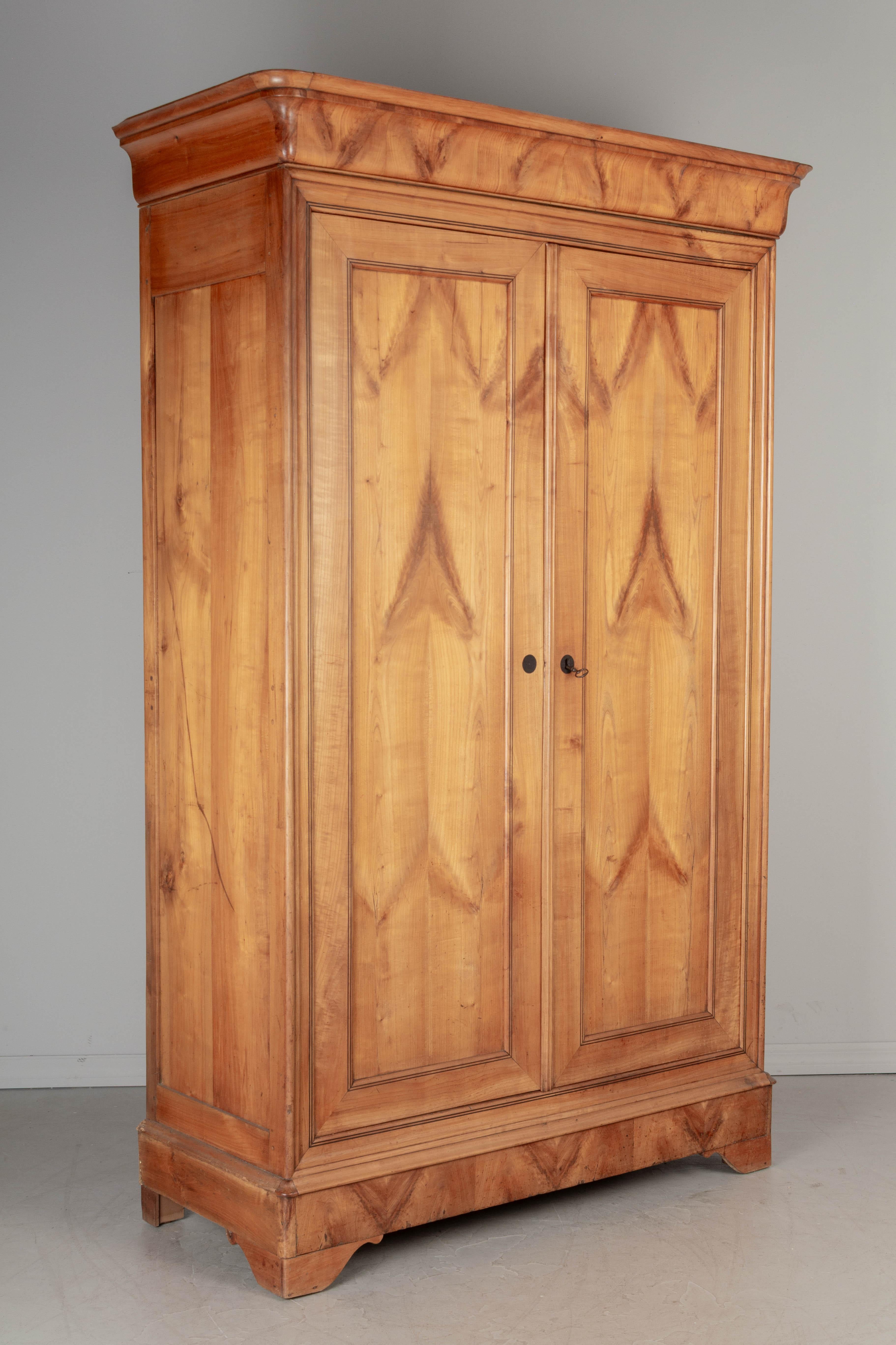 A 19th century French Louis Philippe armoire, or wardrobe, made of solid cherry with beautiful bookmatched wood grain pattern and fine linear inlay around the perimeter of the doors. Interior provides ample storage with two shelves. Working lock and