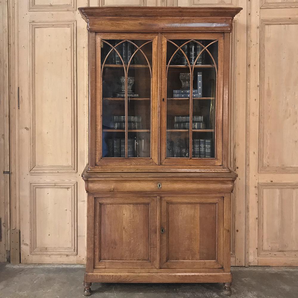 19th Century French Louis Philippe Bookcase is a study in tailored elegance, with signature molded crown and bun feet with two-tiered design that offers display above, a full width drawer in the middle, and storage below. Hand-crafted from solid oak