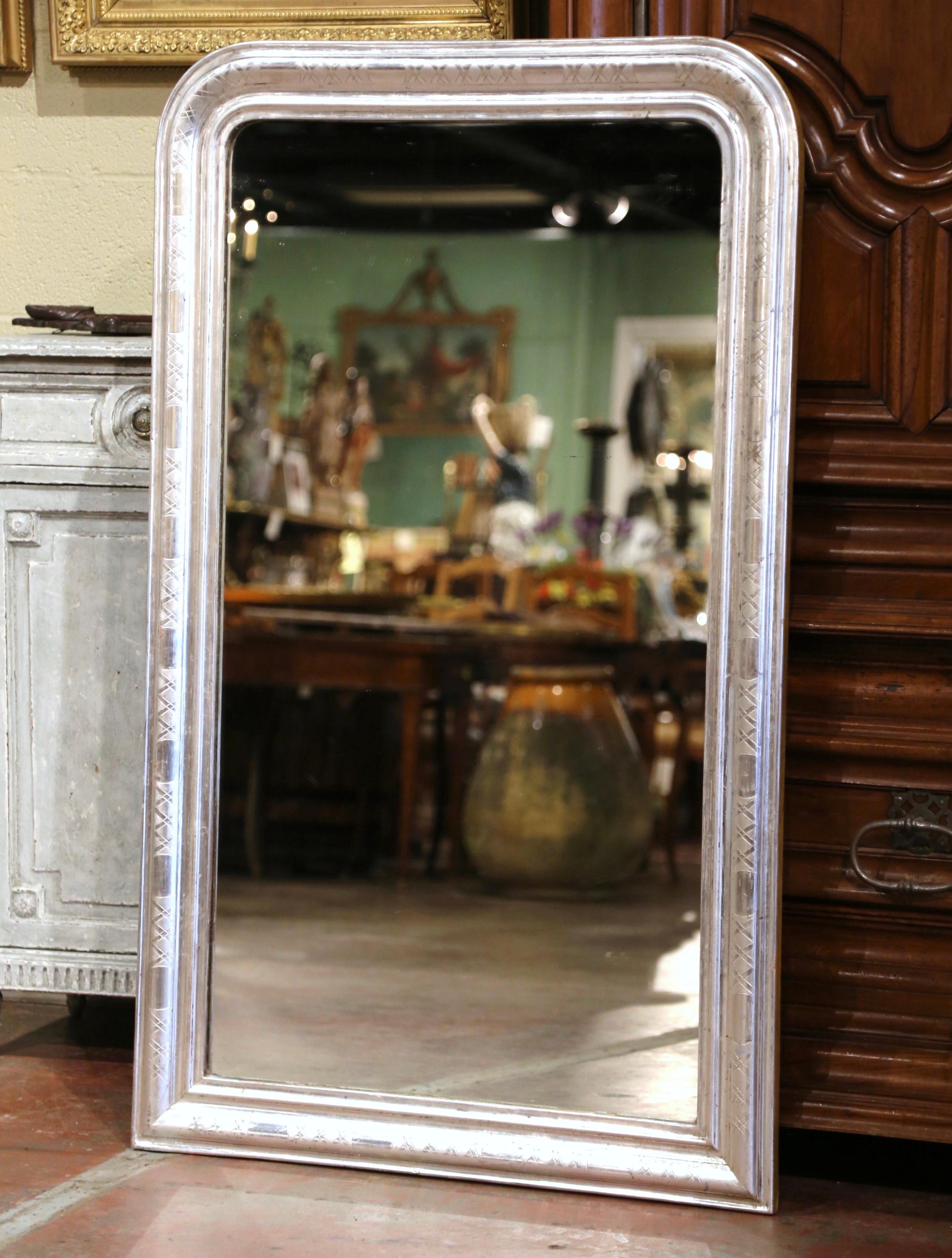 Crafted in the Burgundy region of France, circa 1880, the large antique mirror has traditional, timeless lines with rounded corners. The rectangular frame is decorated with a luxurious silver leaf finish over discrete engraved two-tone geometric