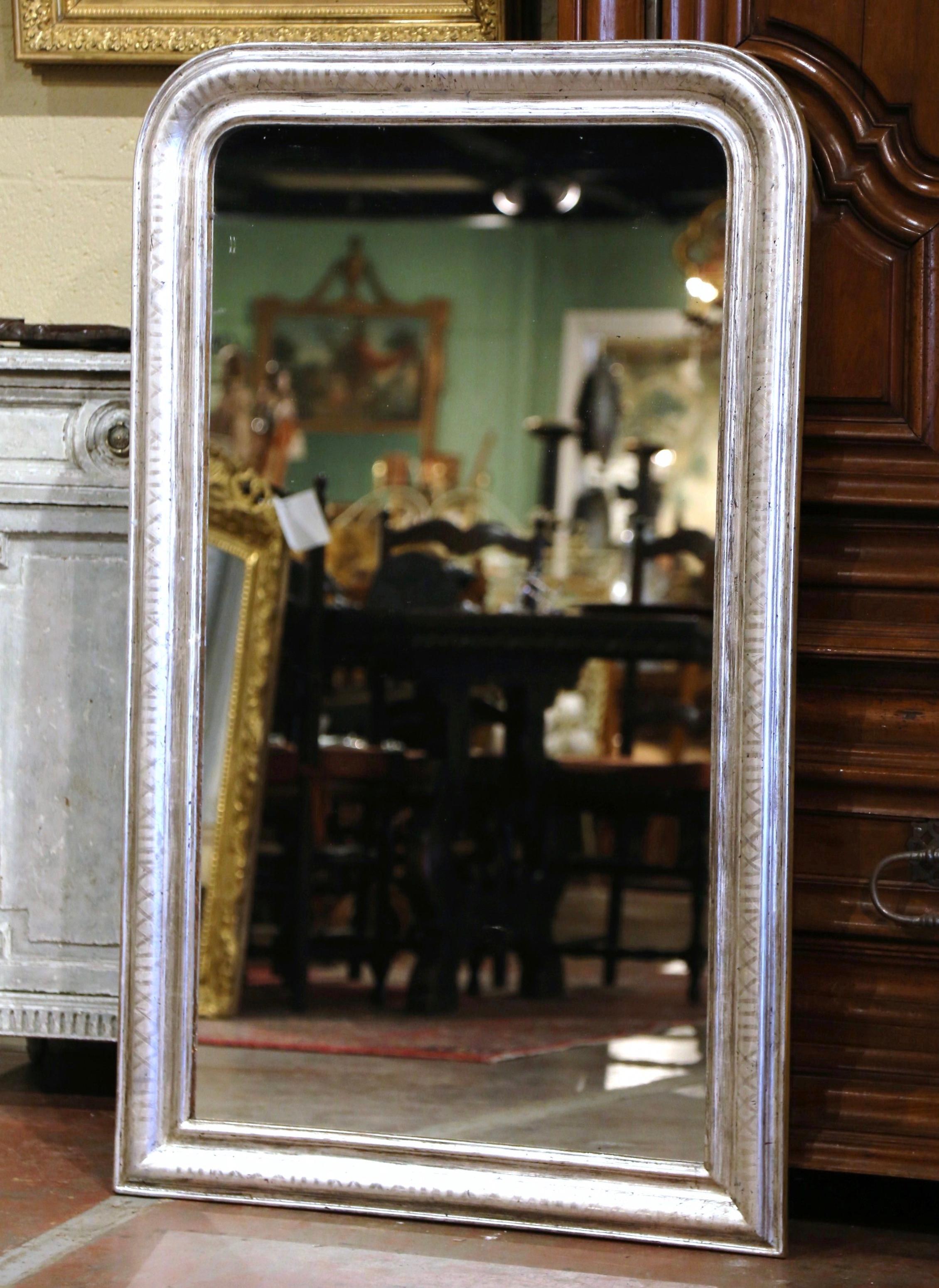 Crafted in the Burgundy region of France, circa 1880, the large antique mirror has traditional, timeless lines with rounded corners. The rectangular frame is decorated with a luxurious silver leaf finish over discrete engraved two-tone geometric