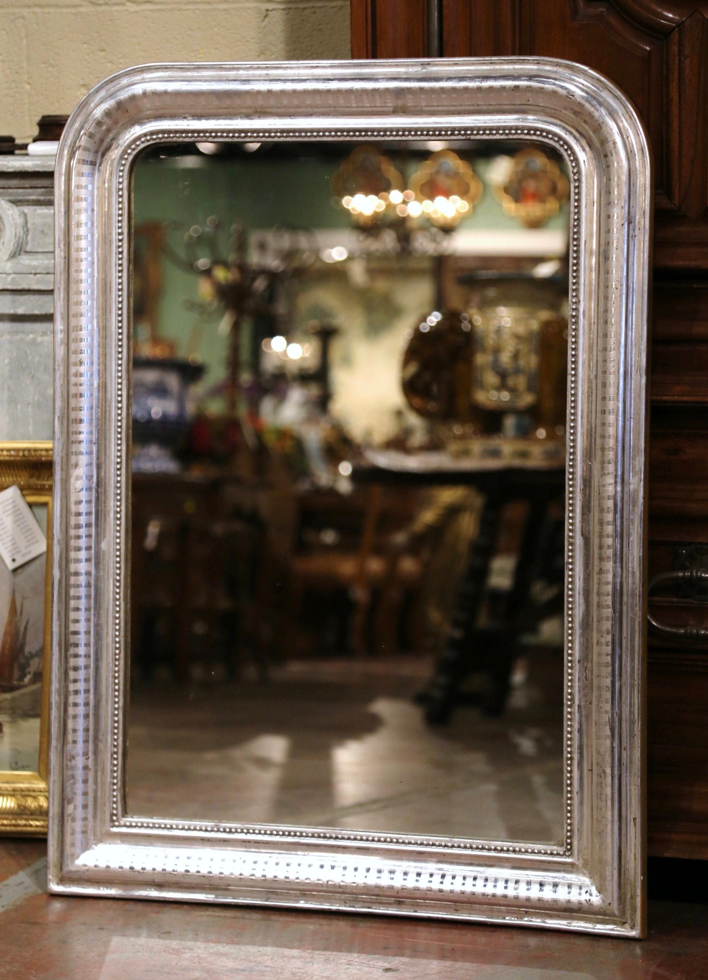 Crafted in the Burgundy region of France, circa 1880, the antique mirror has traditional, timeless lines with rounded corners. The rectangular frame is decorated with a luxurious silver leaf finish over discrete engraved two-tone stripe motif, and