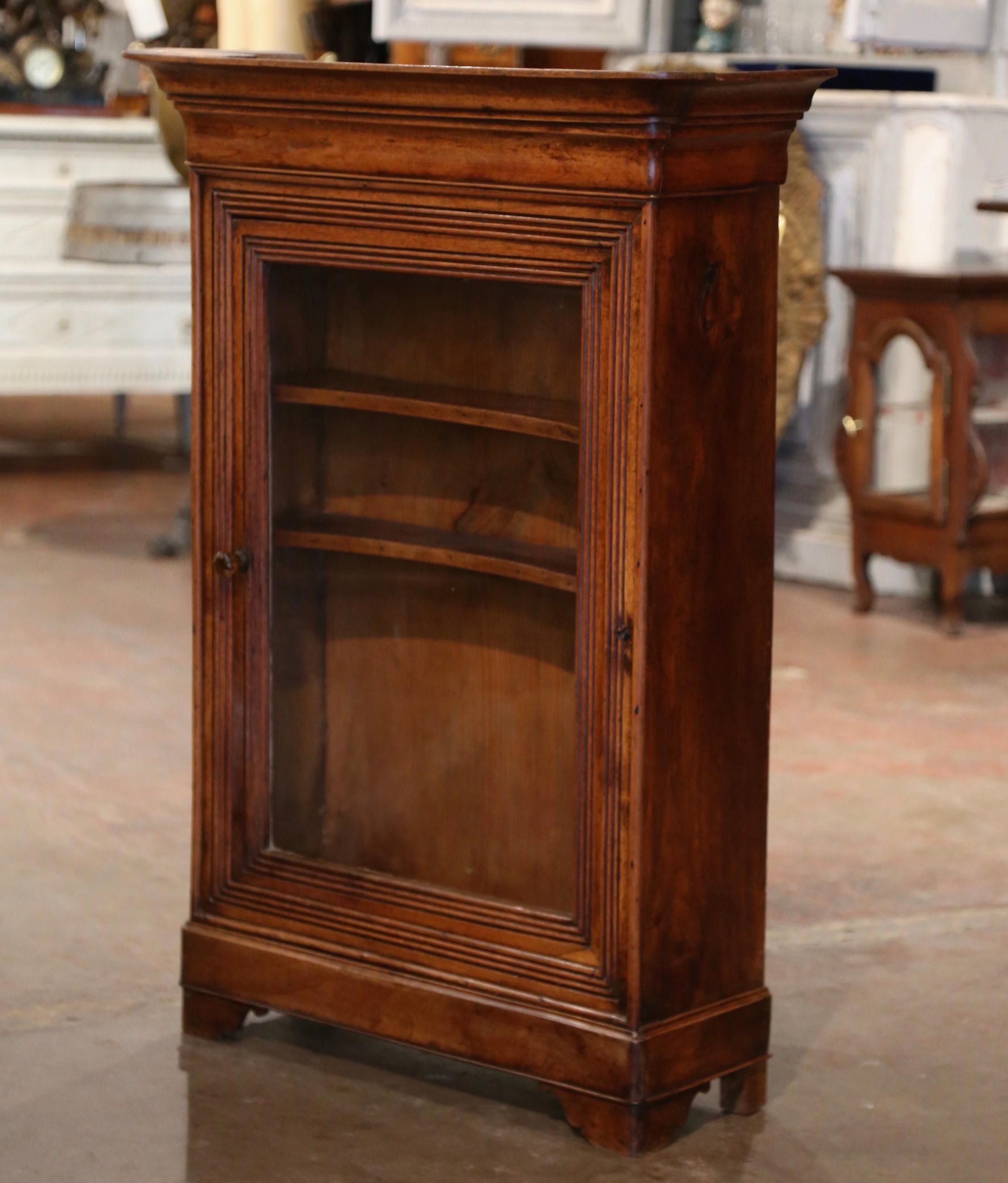 This elegant antique vitrine was crafted in southern France, circa 1850. The wall cabinet with bonnet top, stands on bracket feet, and is decorated with spline motifs on the facade. The curio cabinet features a carved single door dressed with the