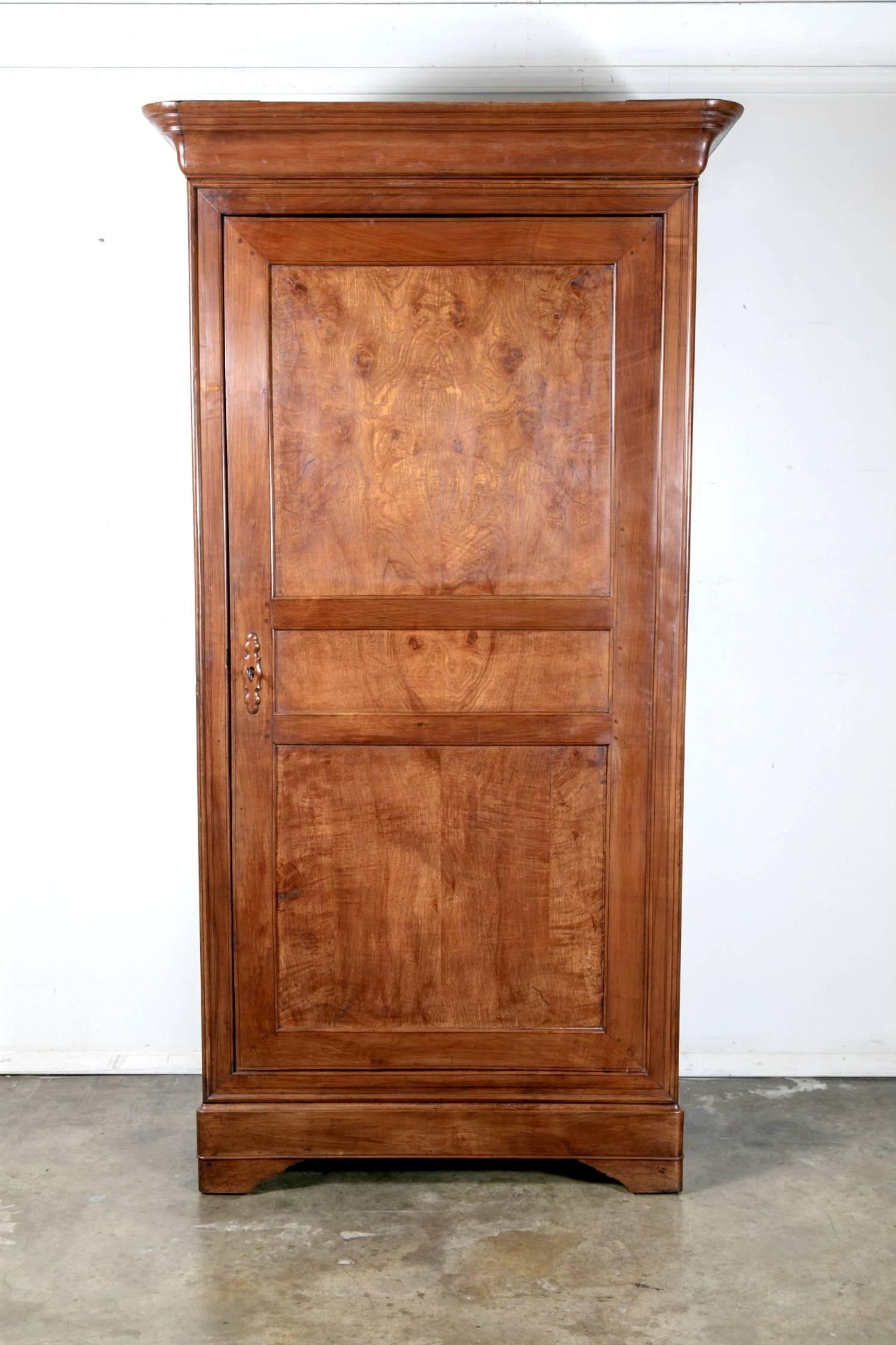 A late 19th century French Louis Philippe style bonnetiere handcrafted in Brittany of cherrywood with a doucine cornice above a burled chestnut door with a bookmatched front, allowing for the uninterrupted enjoyment of the beauty of its wood grain.