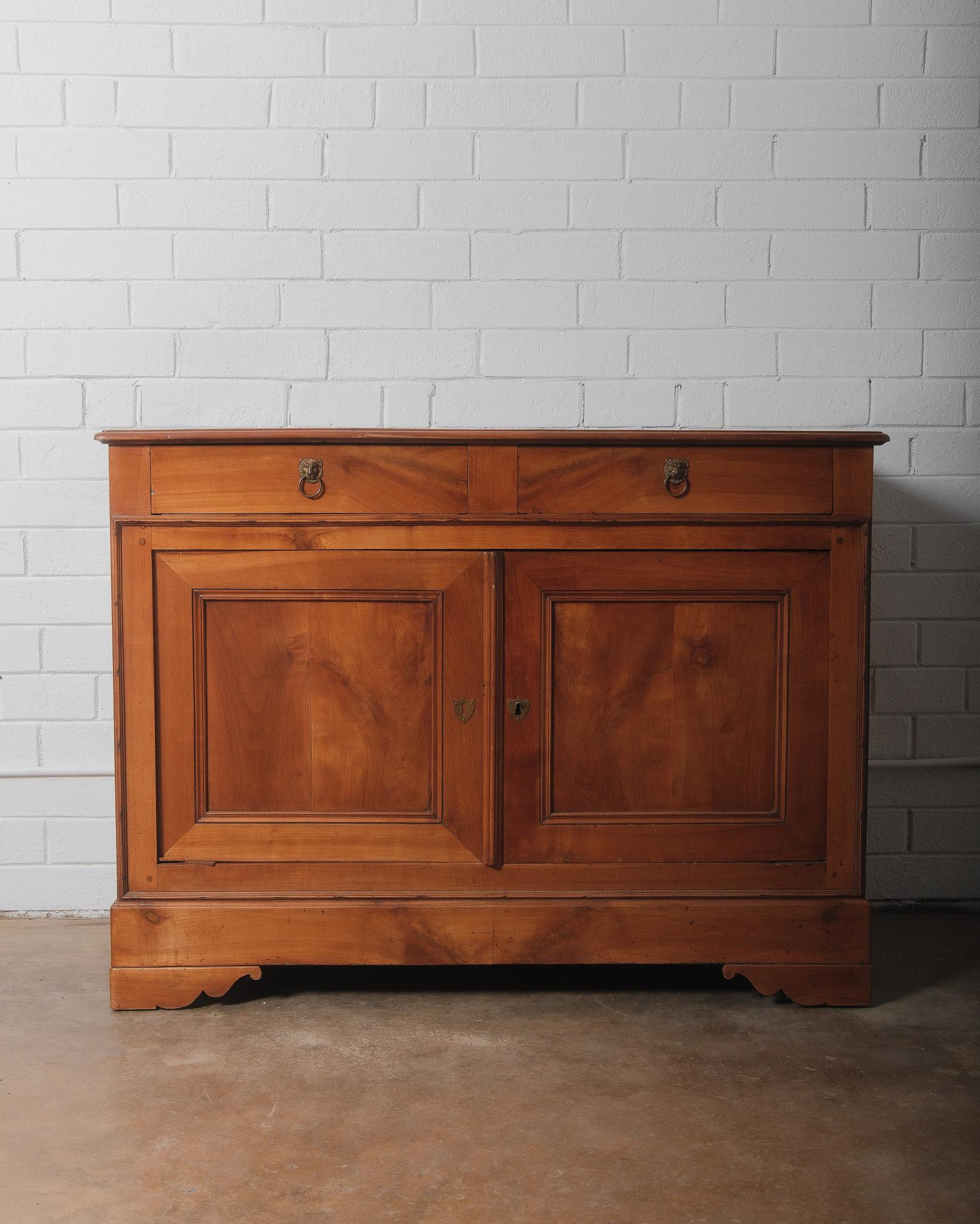 This elegant French Louis Philippe buffet is crafted from warm-toned wood, showcasing clean lines and timeless proportions characteristic of the mid-19th century. Featuring two top drawers with finely detailed brass lion’s head pulls and paneled