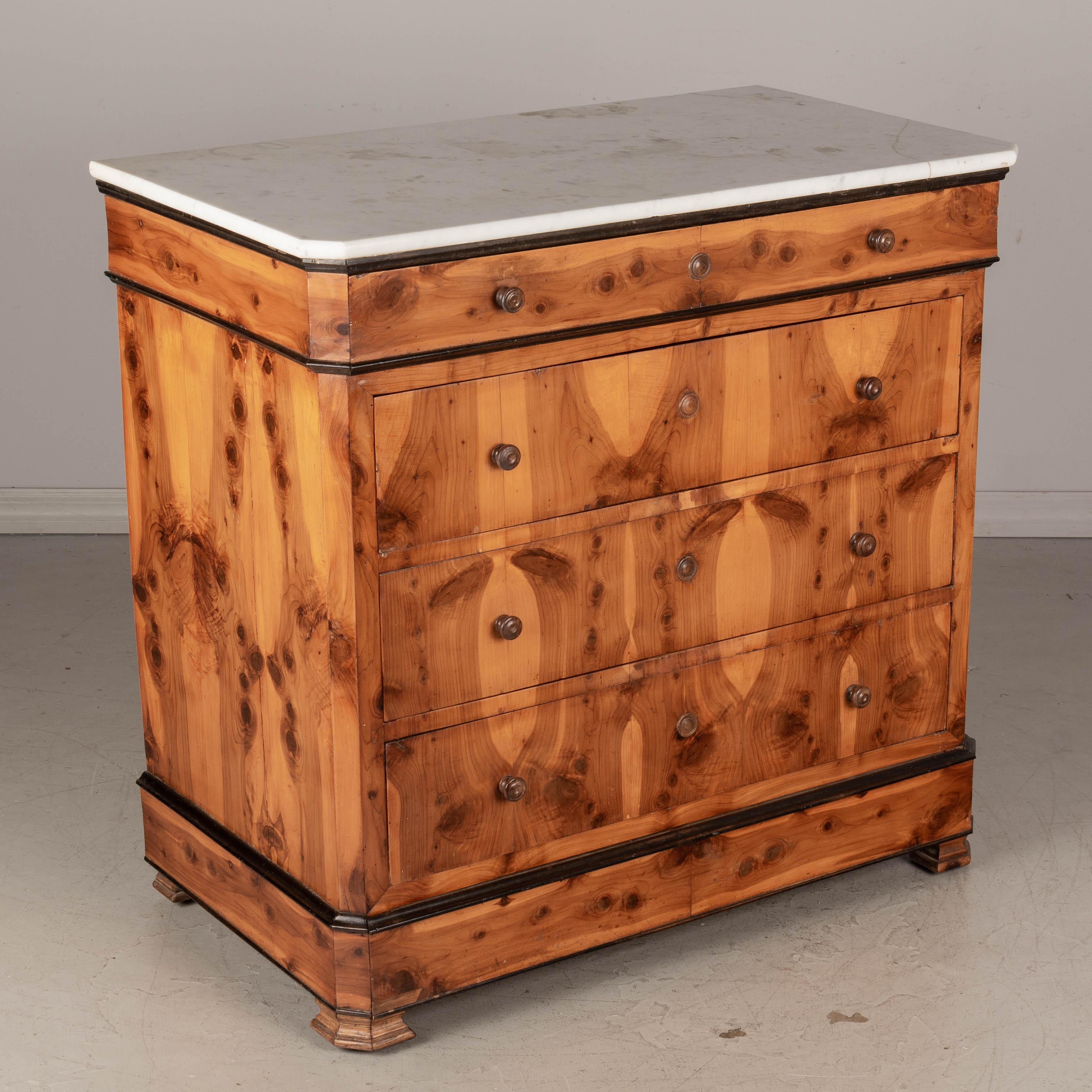 A 19th century French Louis Philippe marble top commode. Nicely patterned book matched cedar veneer over pine with black painted accents. Five dovetailed drawers including a hidden drawer at the plinth. Locks are missing and the wood knobs are not