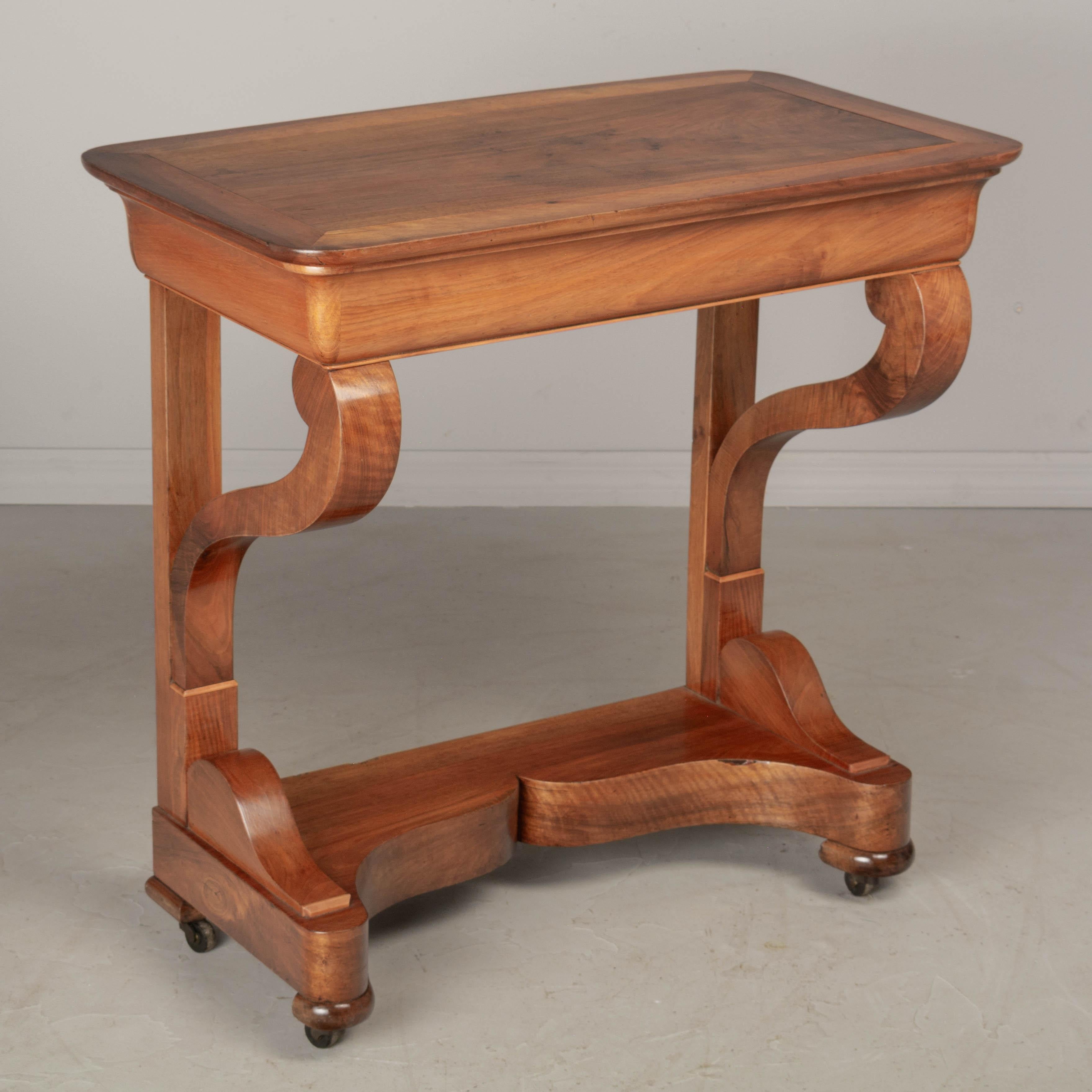 A 19th century French Louis-Philippe console made of solid walnut and veneer of walnut. Sculptural scrolled front legs resting on a curved front plinth base with original castors. Hidden dovetailed drawer opens from the backside. Possibly used as a